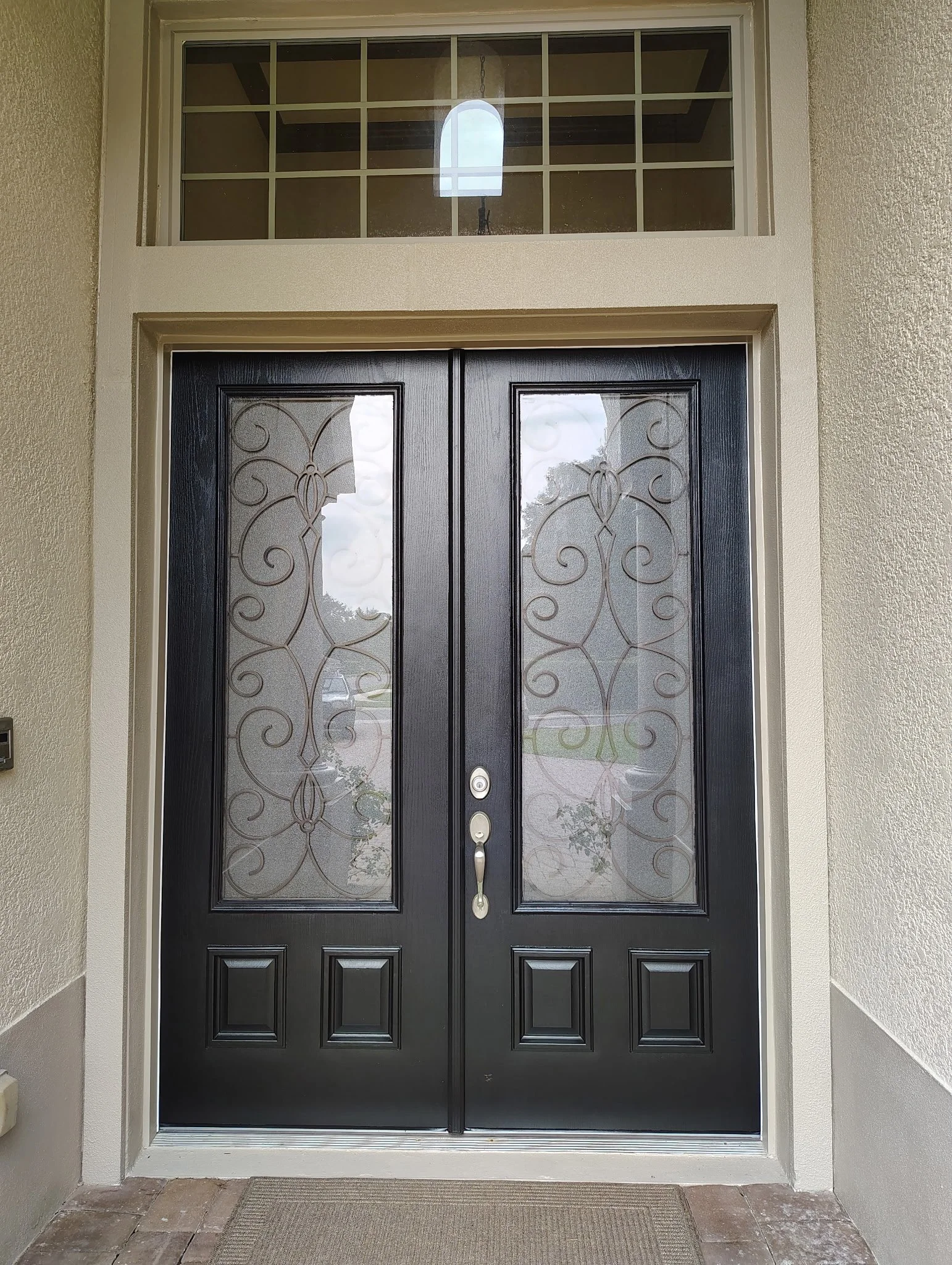 Close finished view of the Sanford home's black double front doors with decorative glass, surrounded by freshly painted neutral stucco and architectural trim.