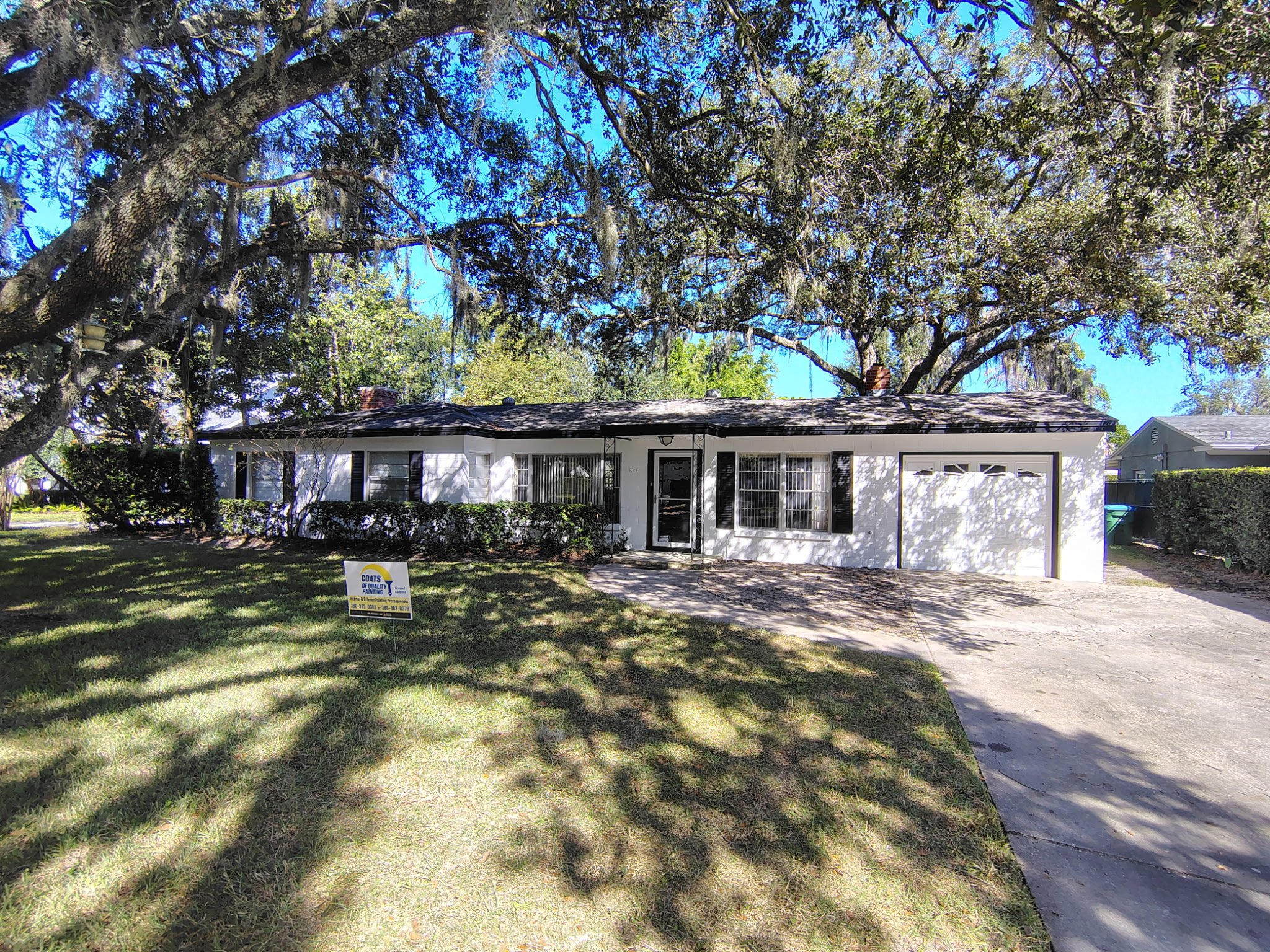Modern white-and-black single-story Winter Park home with front garage, shutters, lawn, and oak tree canopy.