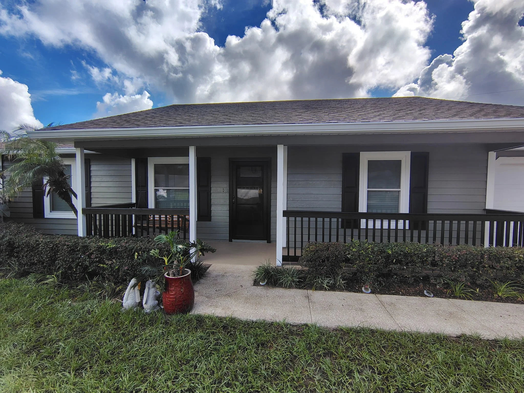 Front porch of an Apopka home after exterior painting with gray-green siding, bright white posts and window trim, dark shutters and contrasting porch railings.