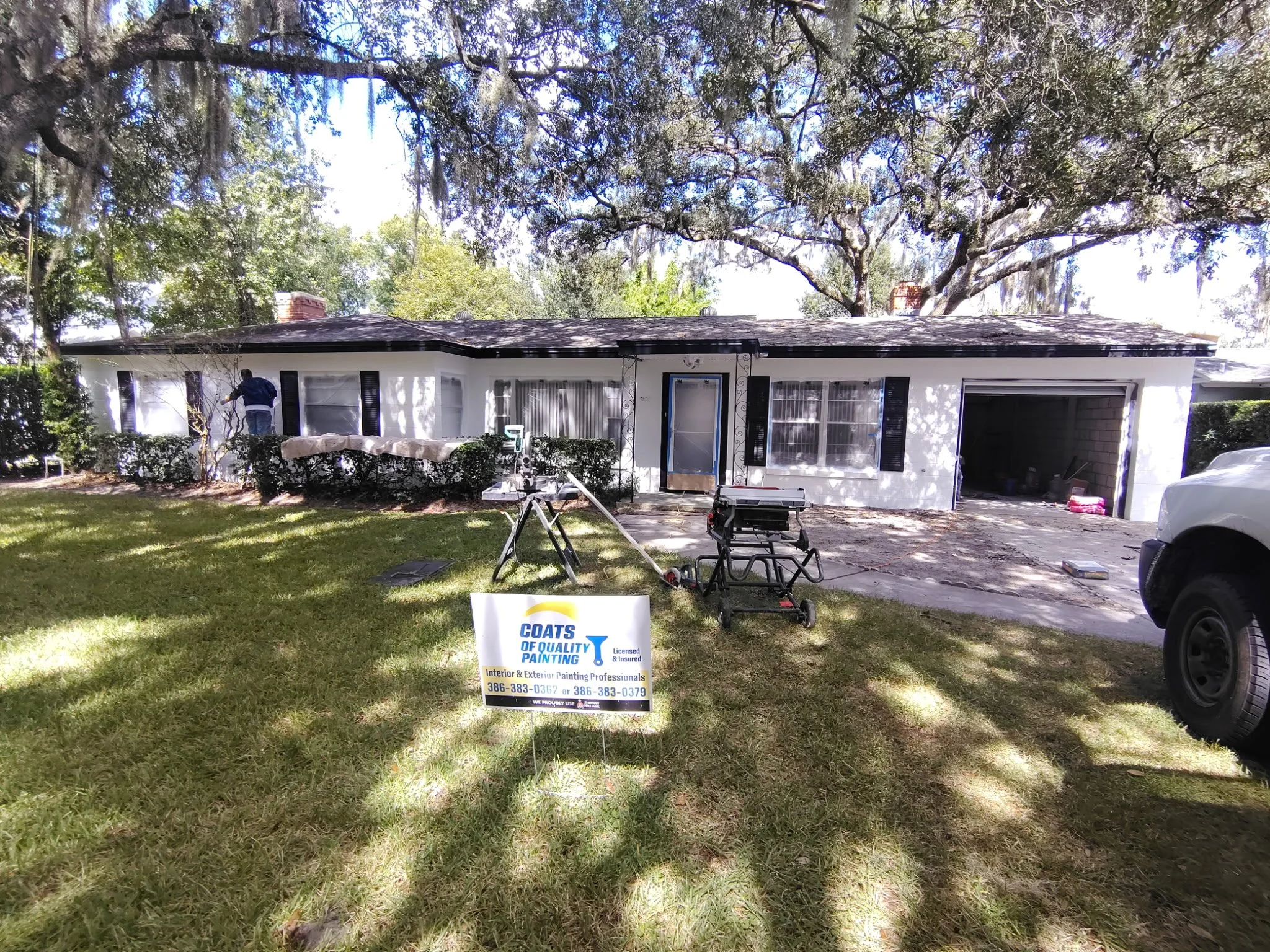 White concrete block wall with black shutters, dark fascia, greenery, and ladder at a Winter Park painting project.