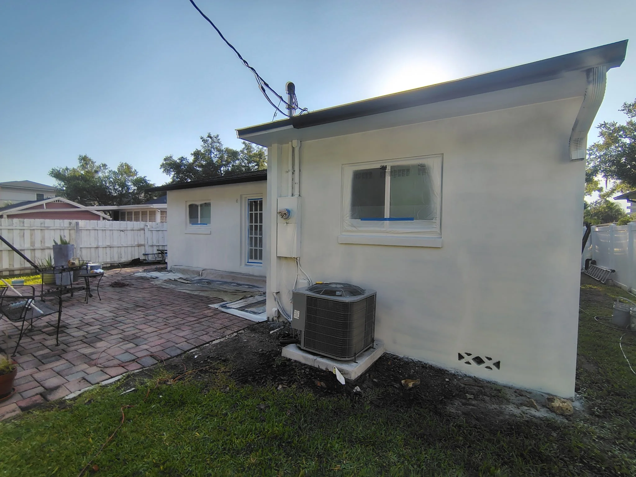 This back patio photo shows the exterior stucco walls, masked windows, covered patio areas, and trim prep during a Winter Park, FL home painting project by Coats of Quality Painting. The project uses Sherwin-Williams Origami White on the walls and Pu