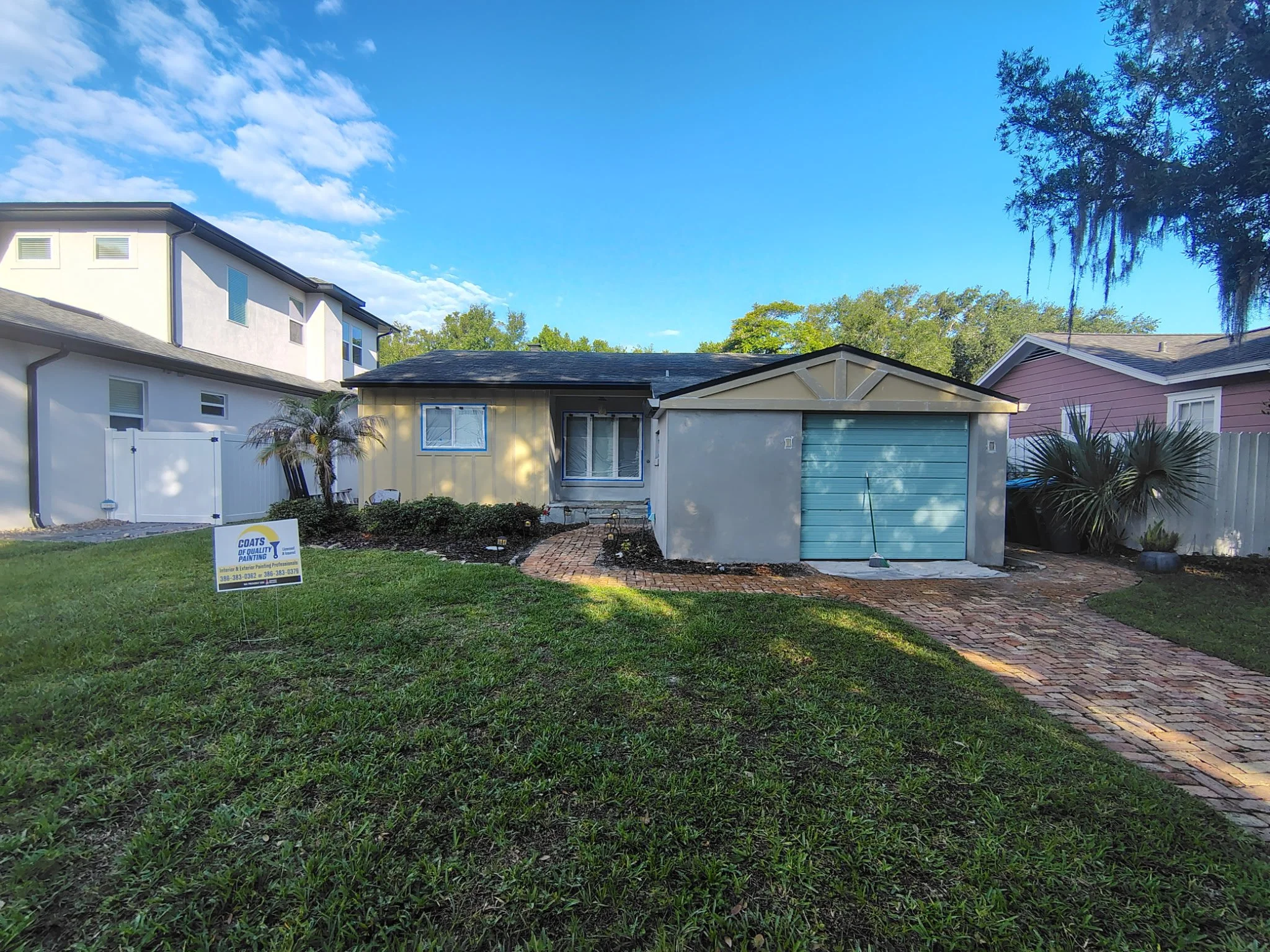 This full front view shows the current Winter Park, FL exterior painting project by Coats of Quality Painting. The home features stucco, Hardie board siding, garage trim, masked windows, and a fresh Sherwin-Williams color update using Origami White w