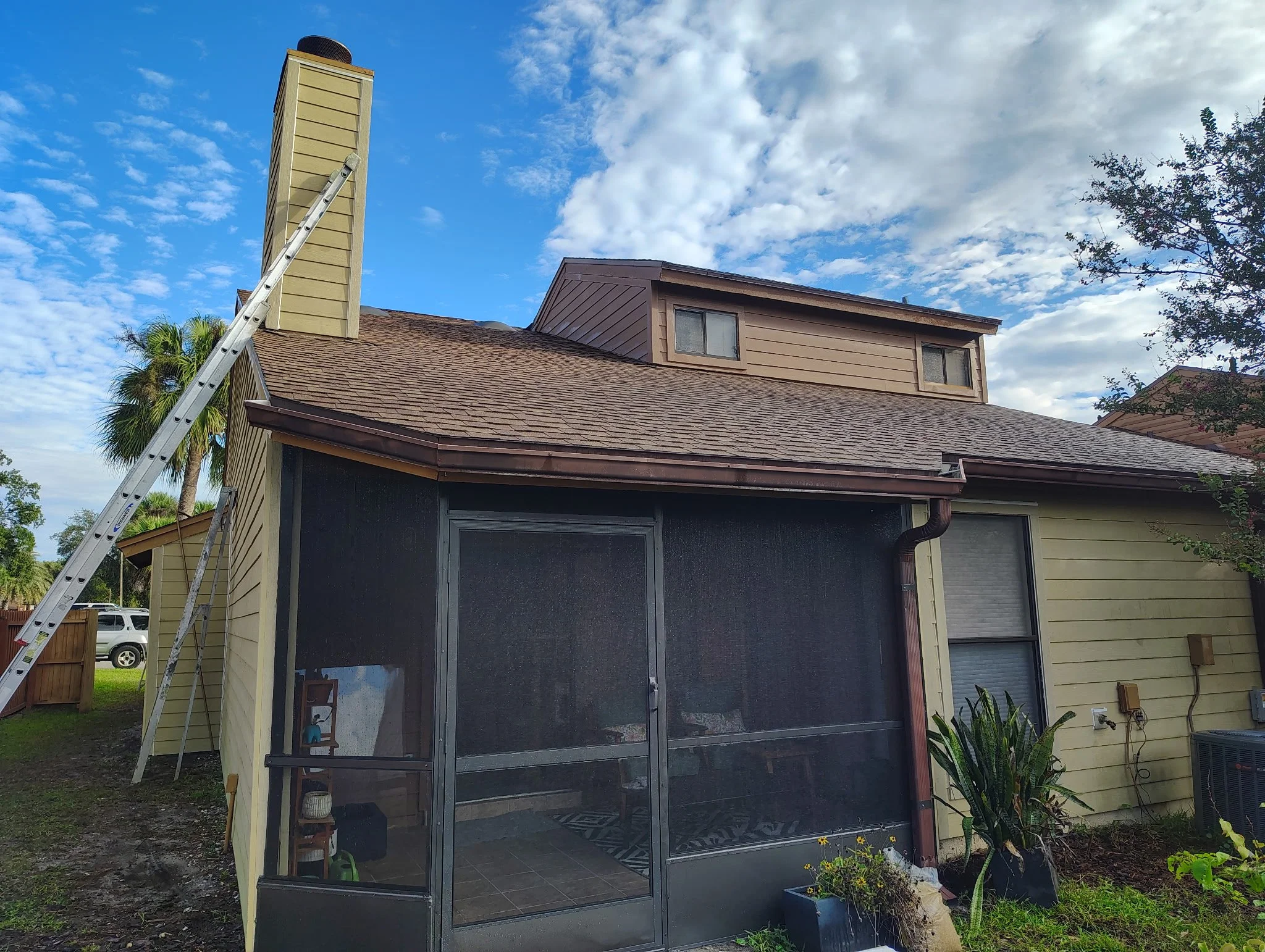 Rear screened patio, roofline, chimney, beige siding, and painting access ladders at a house in Altamonte Springs, FL.