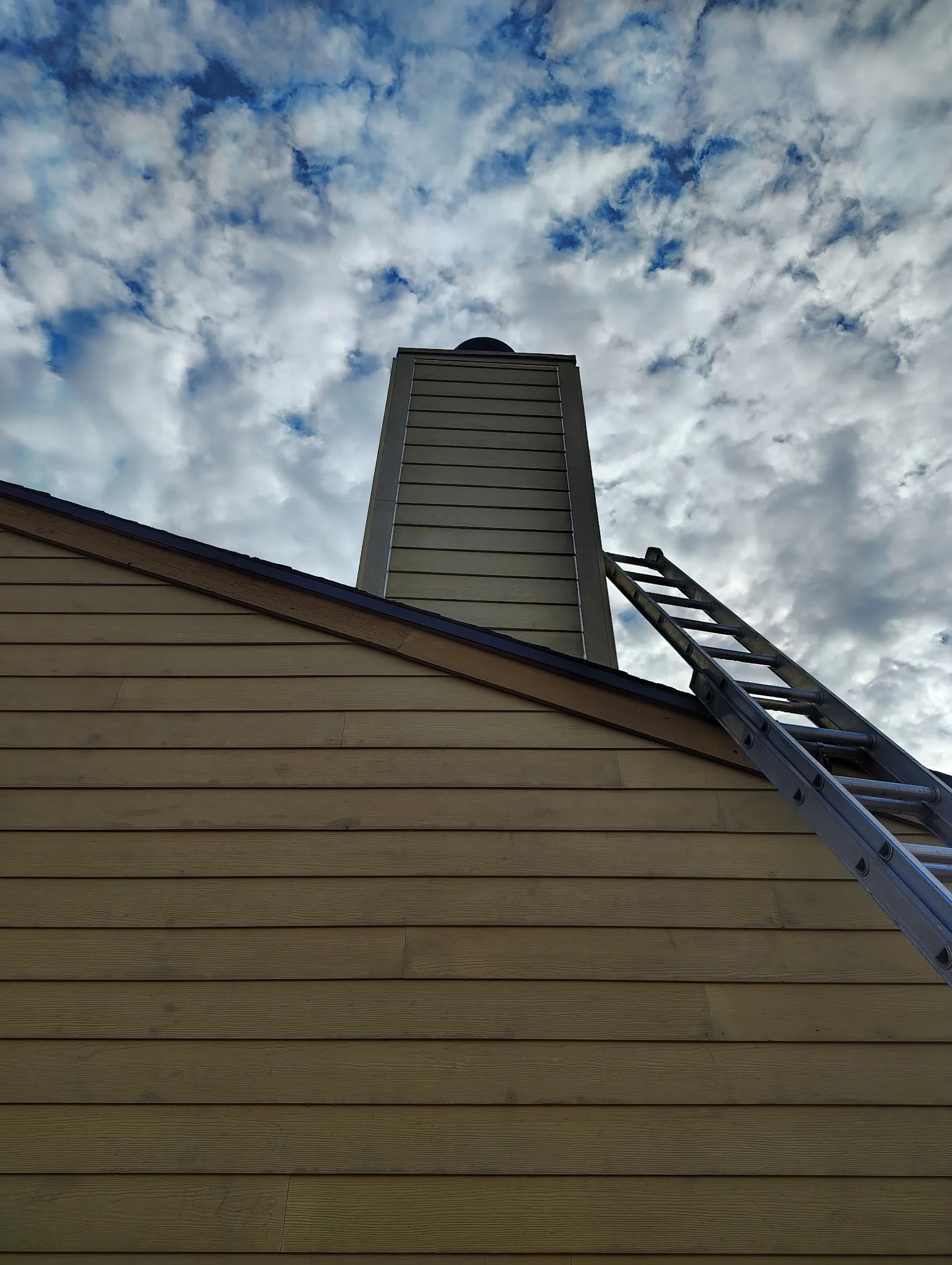 Upper exterior siding and tall chimney with an extension ladder at a residential painting project in Altamonte Springs, Florida.