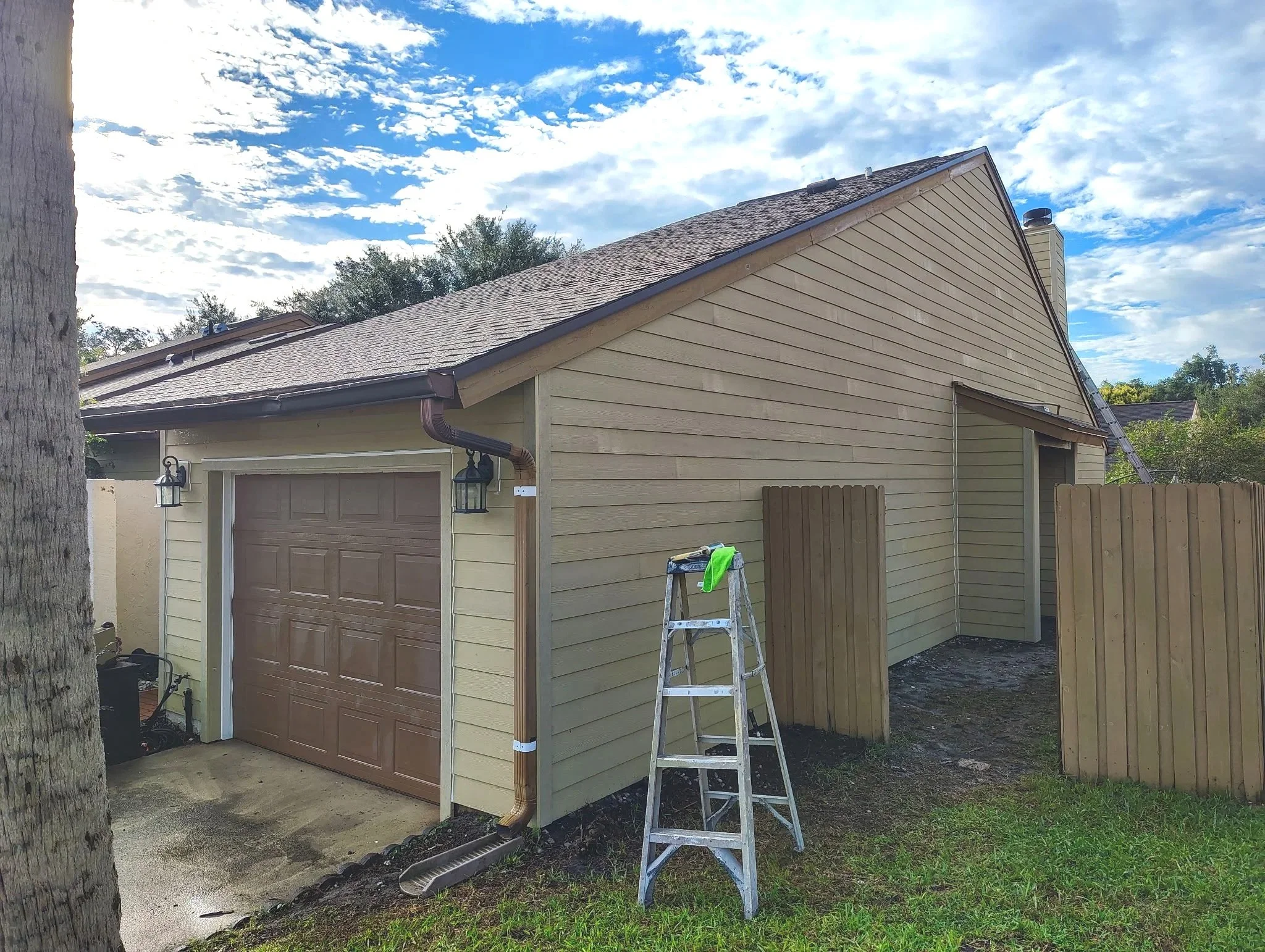 Side view of an Altamonte Springs home with beige horizontal siding, a brown garage door, and exterior trim before repainting.