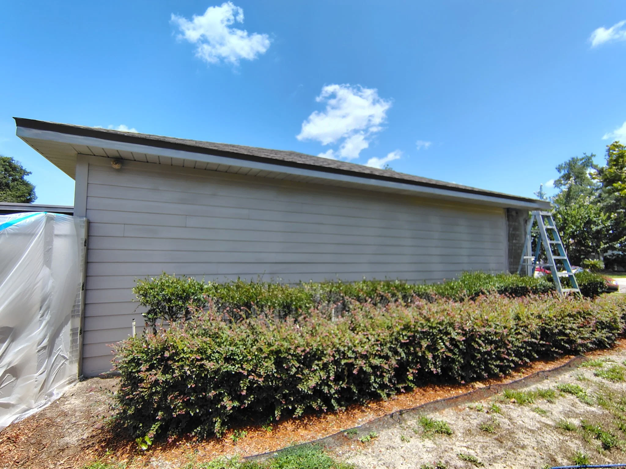 Back of Ocoee home with yellow siding and porch windows masked for exterior painting