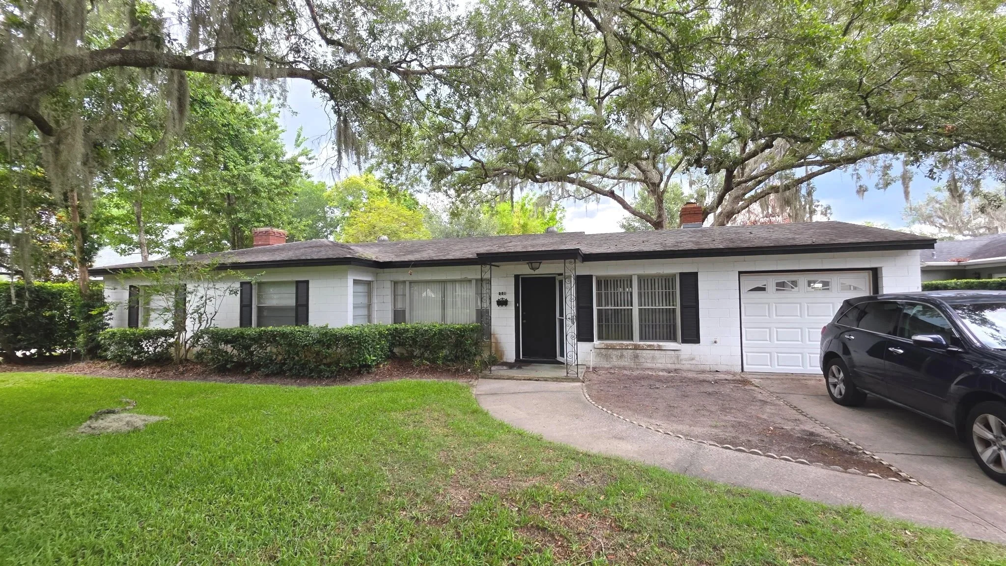 Before photo of a Winter Park single-story house with white masonry walls, black shutters, garage, and visible weather stains.