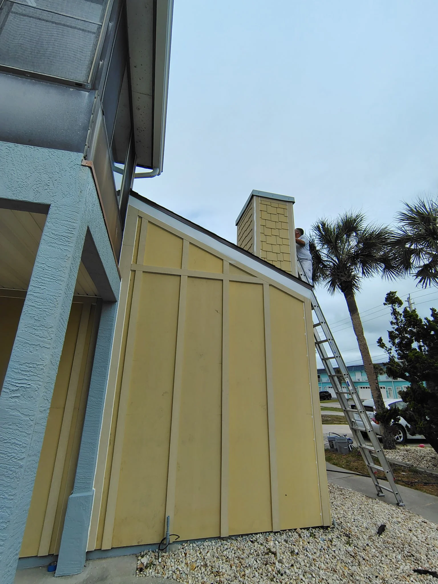 Painter on ladder working on chimney during exterior painting project in South Daytona Florida