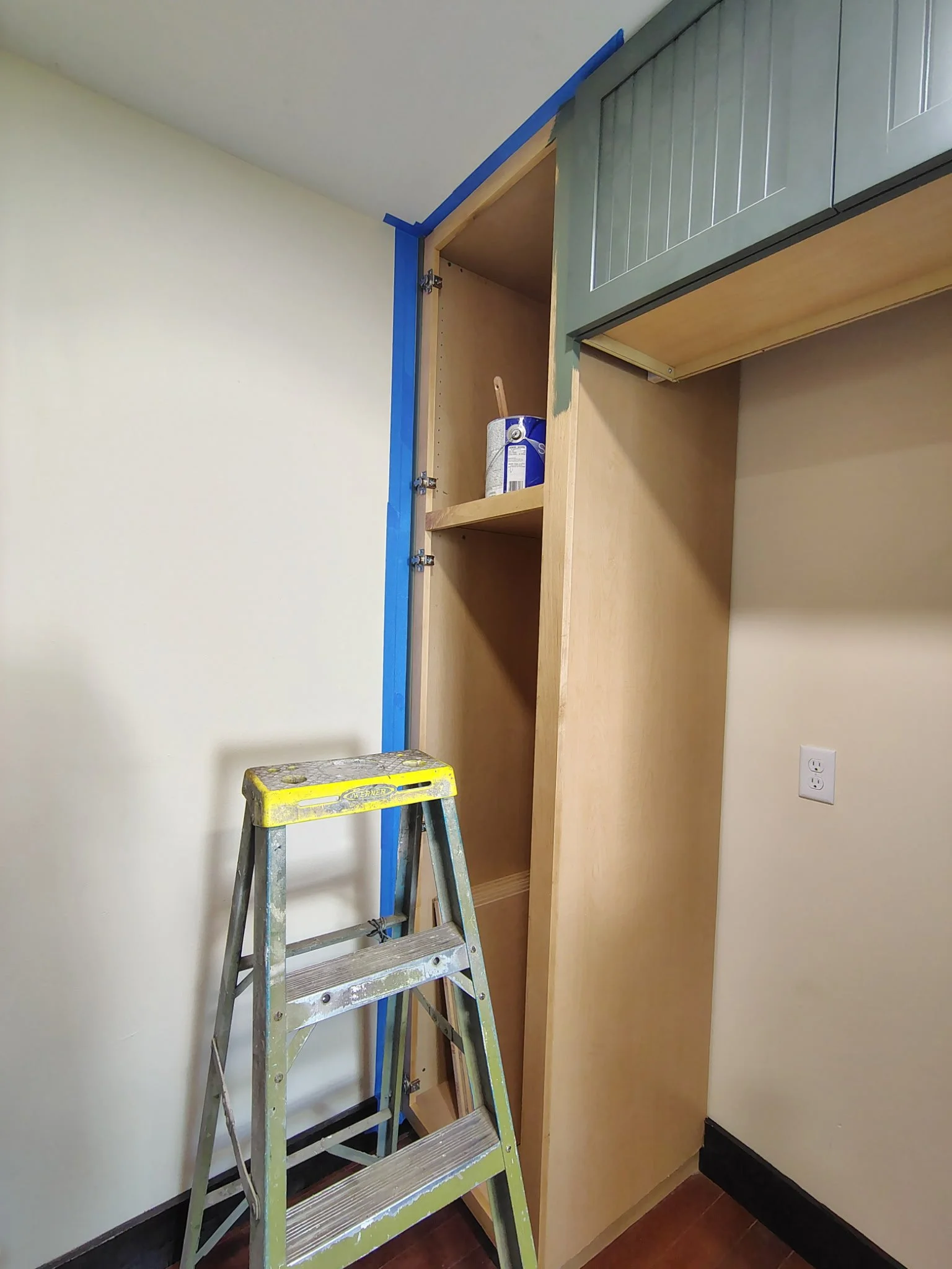 Upper cabinet painting in progress with blue tape and ladder during a Pierson FL cabinet refinishing project.