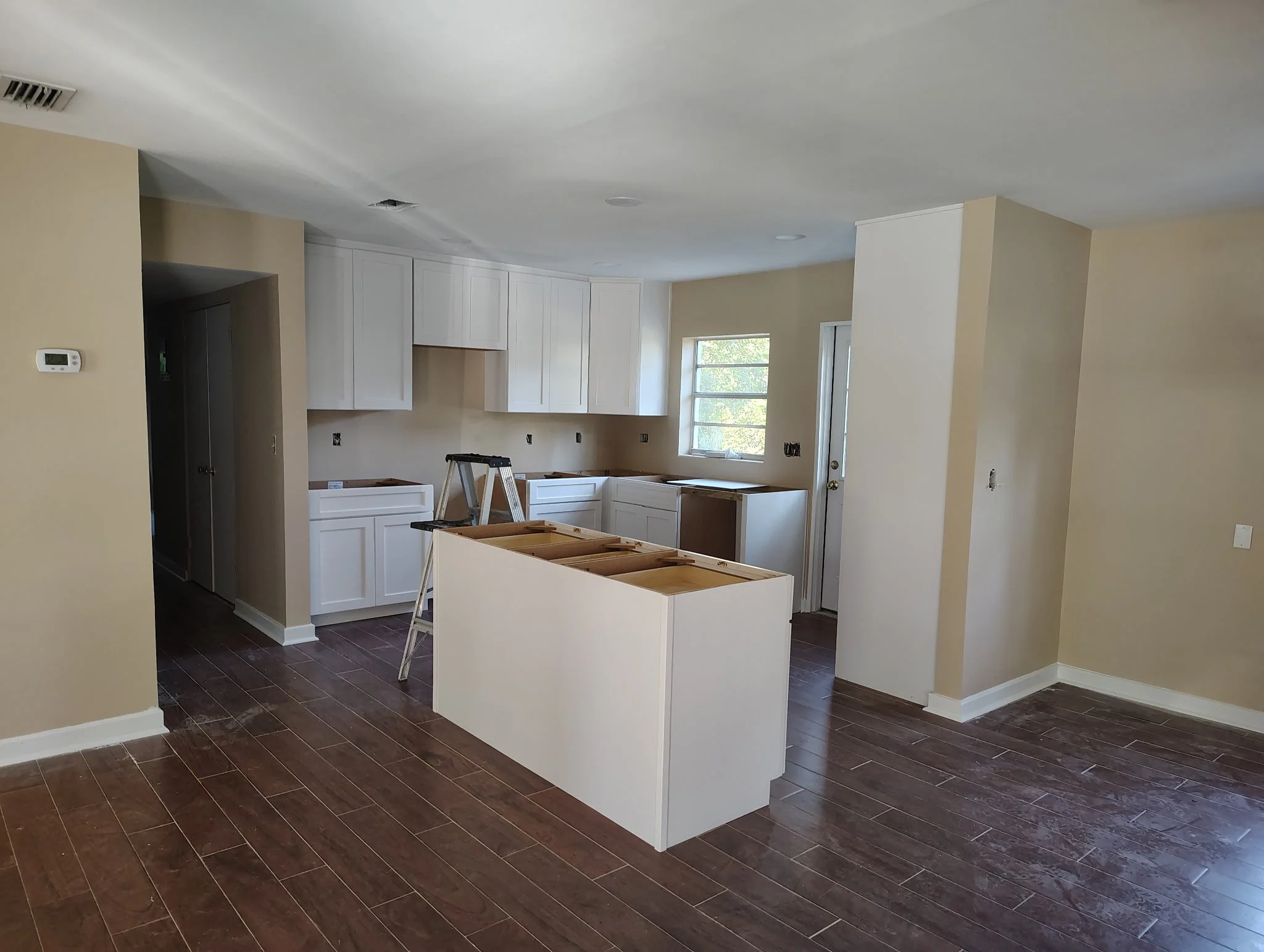 Open kitchen and living area with beige walls, white cabinets, white ceiling, and dark wood-look flooring in Winter Park, FL.