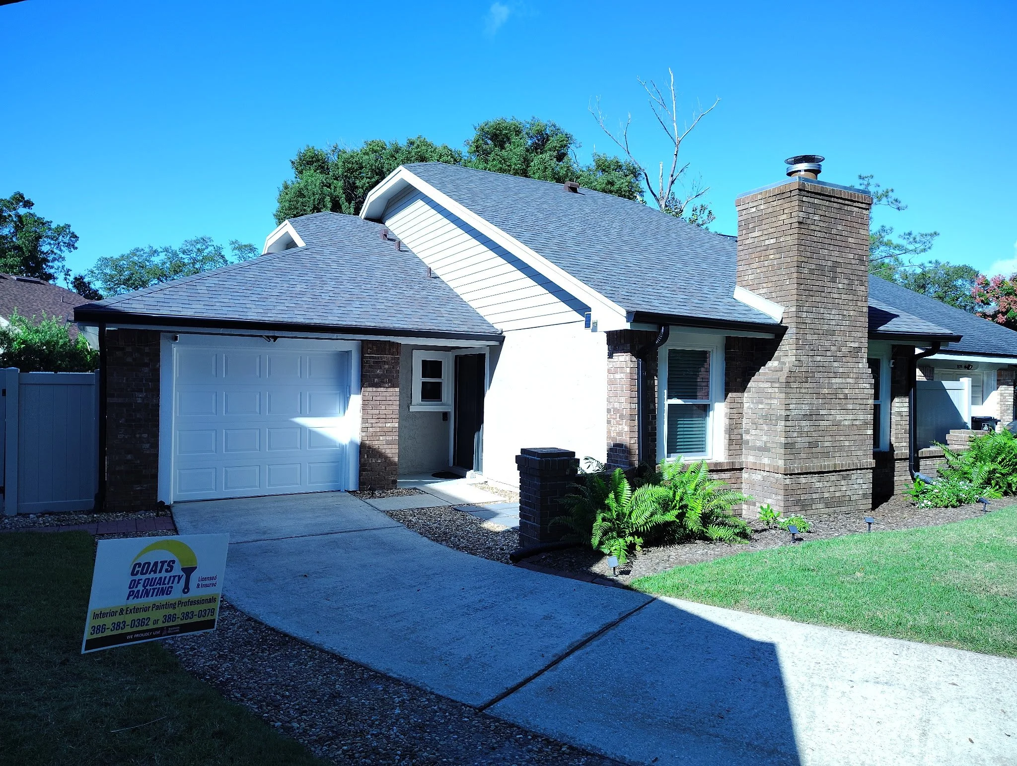 Side of an Orlando house after exterior painting with light neutral gable siding, white fascia, natural brick chimney, and white privacy fence.