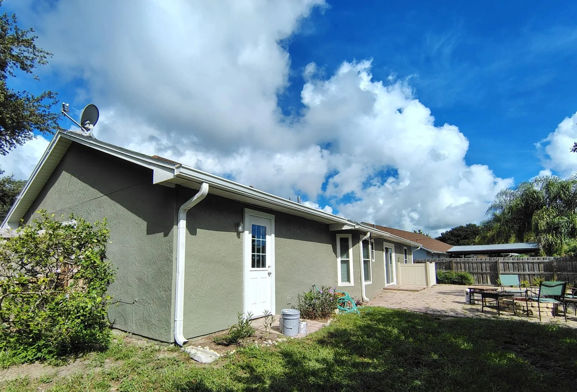 Rear and side view of an Apopka home after professional exterior painting, with refreshed gray-green stucco, bright white doors, trim, gutters and windows.