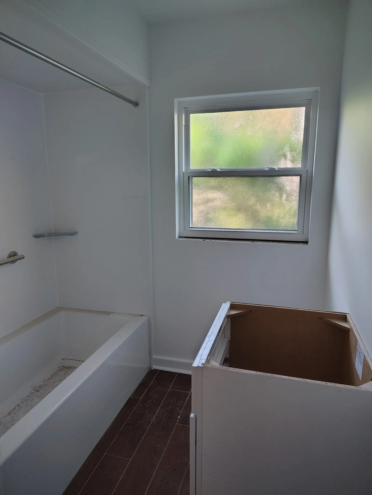 Winter Park bathroom with white walls, bathtub, frosted window, and dark wood-look flooring during an interior update.