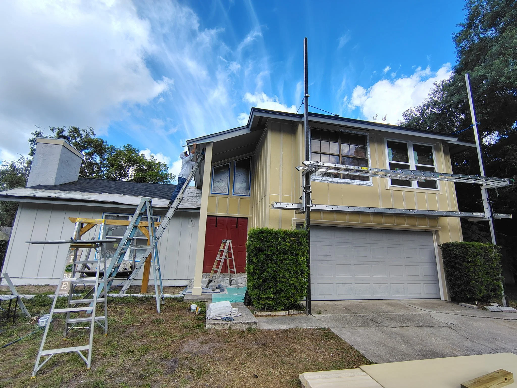 Front view of Longwood home exterior painting project with protected windows, garage, ladders, and trim preparation.