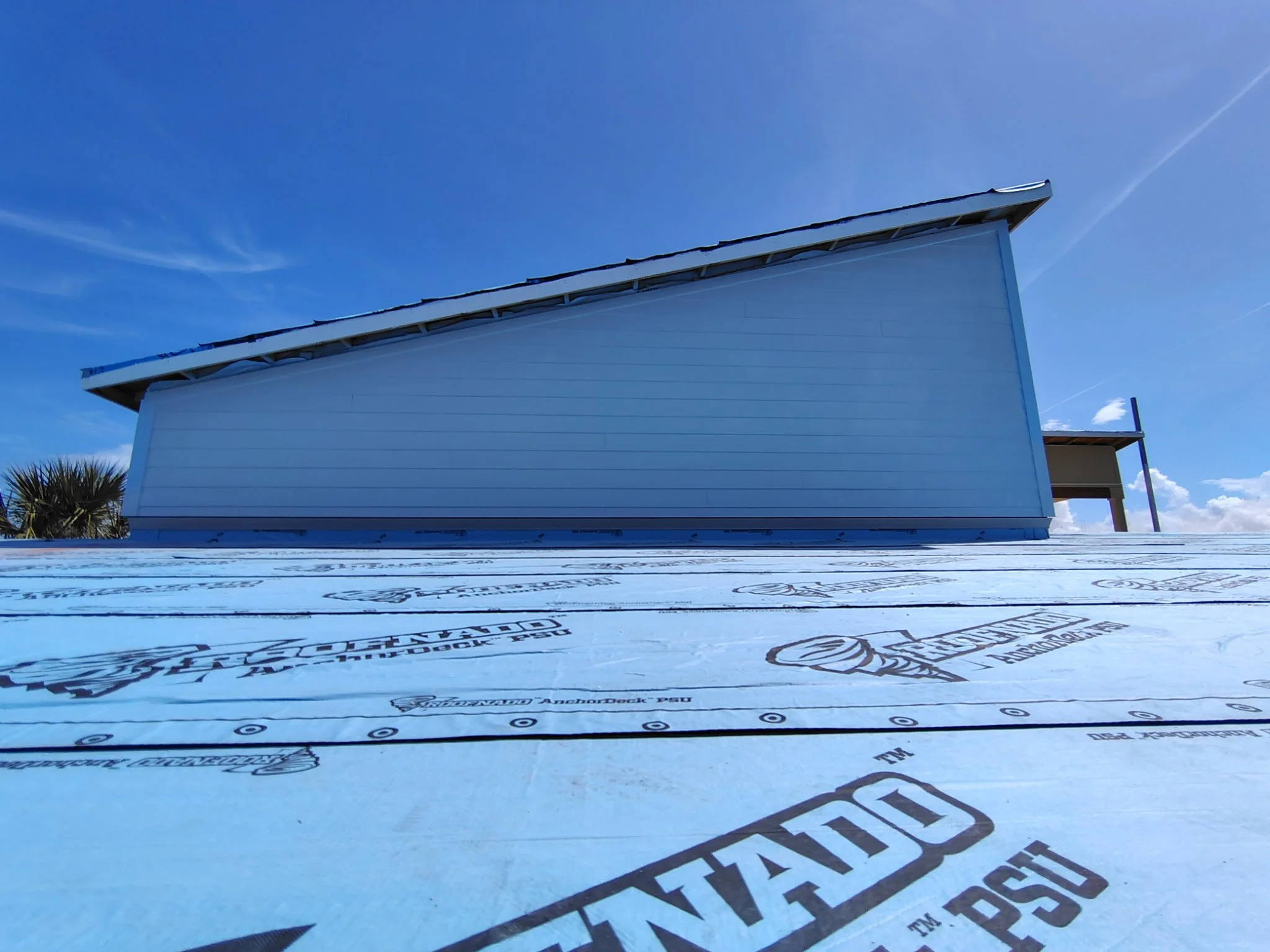 Exterior house painting prep on Hardie board siding in South Daytona with roof underlayment and clear blue sky