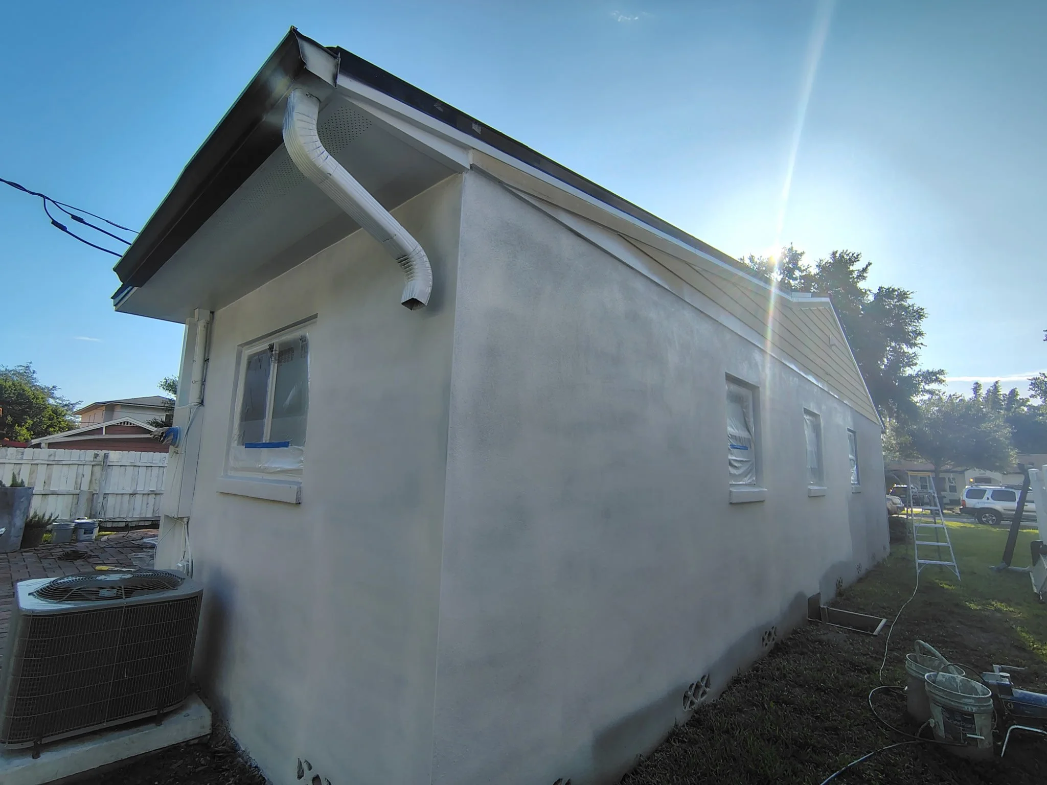 This rear view shows stucco wall preparation, masked windows, trim detail, and exterior paint setup on a Winter Park, FL home. Coats of Quality Painting is preparing the surface for Sherwin-Williams SuperPaint Exterior Satin in Origami White with Pur