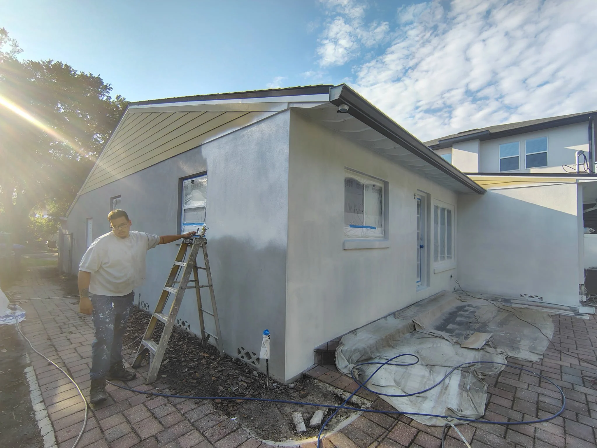 This photo shows the Coats of Quality Painting team actively working on a Winter Park, FL exterior painting project. The home includes stucco and Hardie board siding, with protected windows, covered pavers, and Sherwin-Williams exterior paint being a