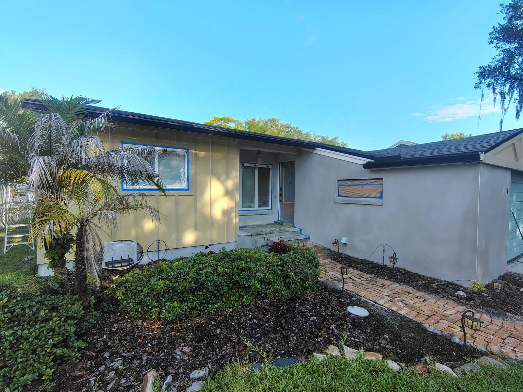 This photo shows the front entry of a Winter Park, FL exterior stucco and Hardie board painting project by Coats of Quality Painting. Windows and doors are masked, surfaces are being prepared, and the home is being updated with Sherwin-Williams Origa