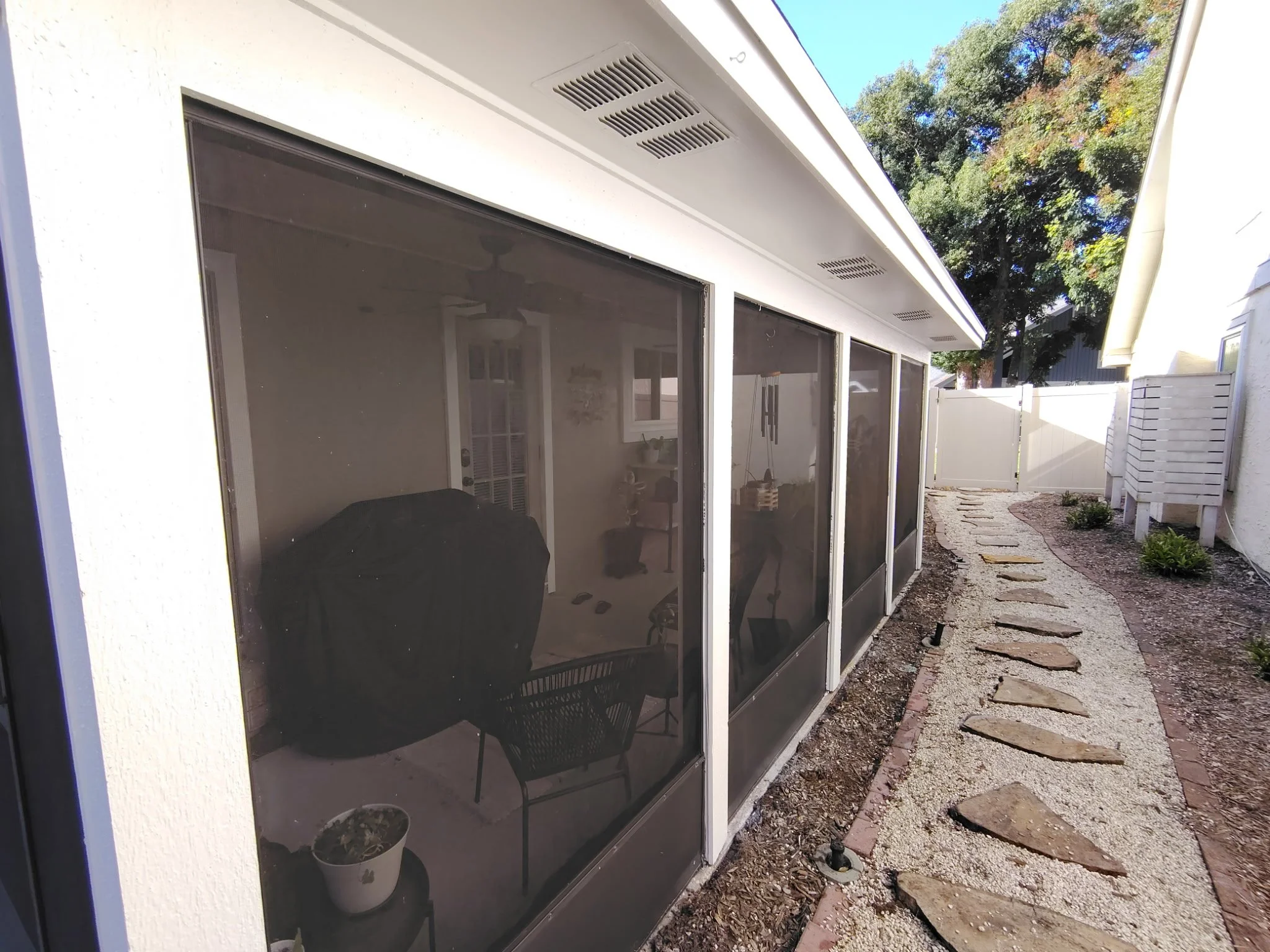 Screened outdoor enclosure with light exterior framing, white soffits, and landscaped stepping-stone pathway after an Orlando house repaint.