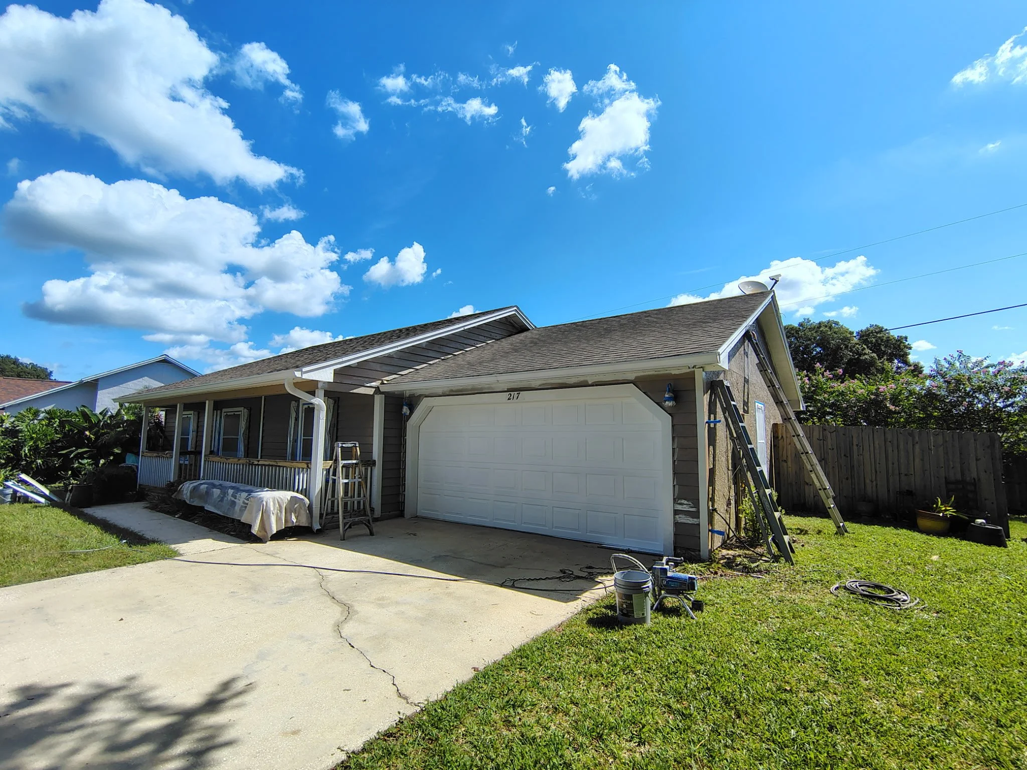 Angled front view of an Apopka residence showing exterior painting preparation around the garage, siding, trim and covered porch before final coating.