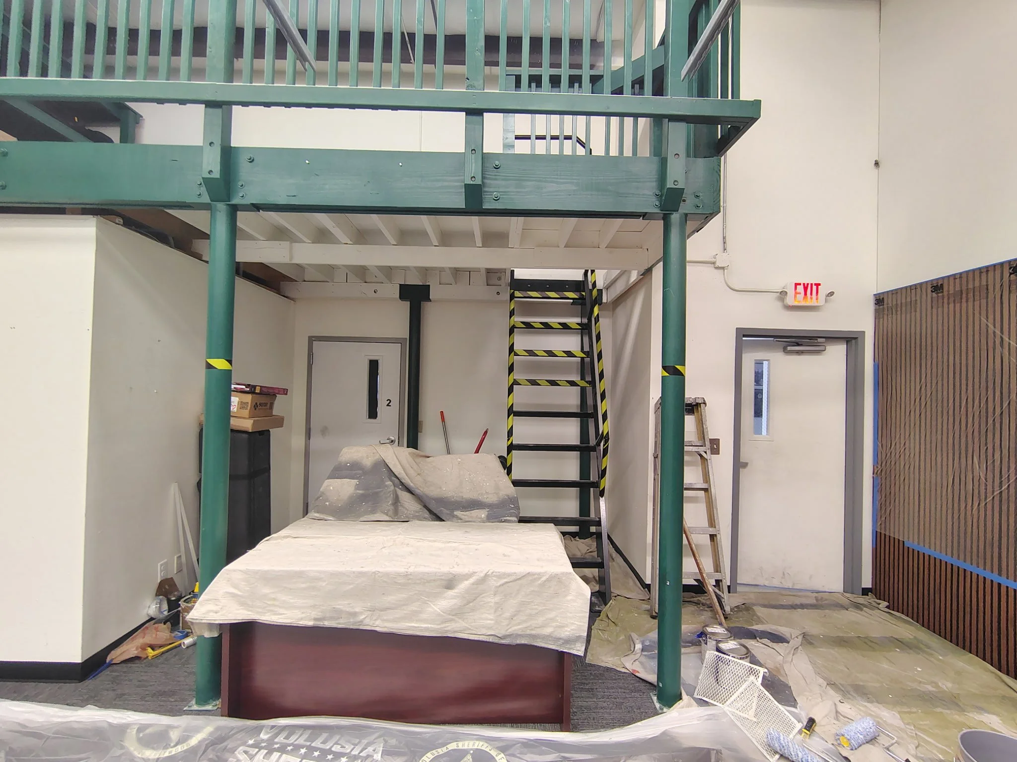 SWAT hangar-style interior painting prep in Volusia County with covered desk, protected flooring, staircase, and tall walls.
