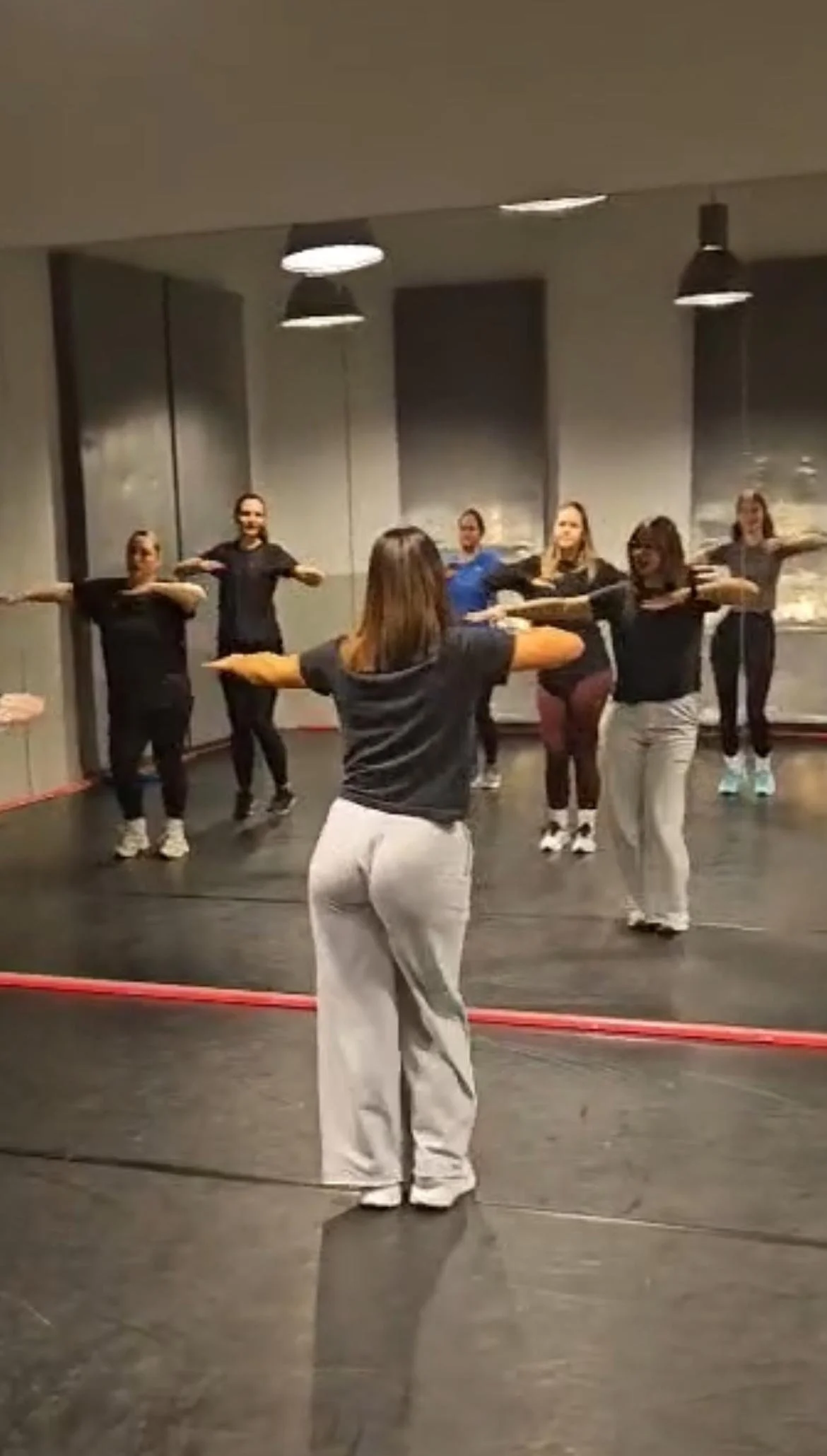 Group of women in workout clothes participating in a dance or exercise class in a studio, following an instructor.