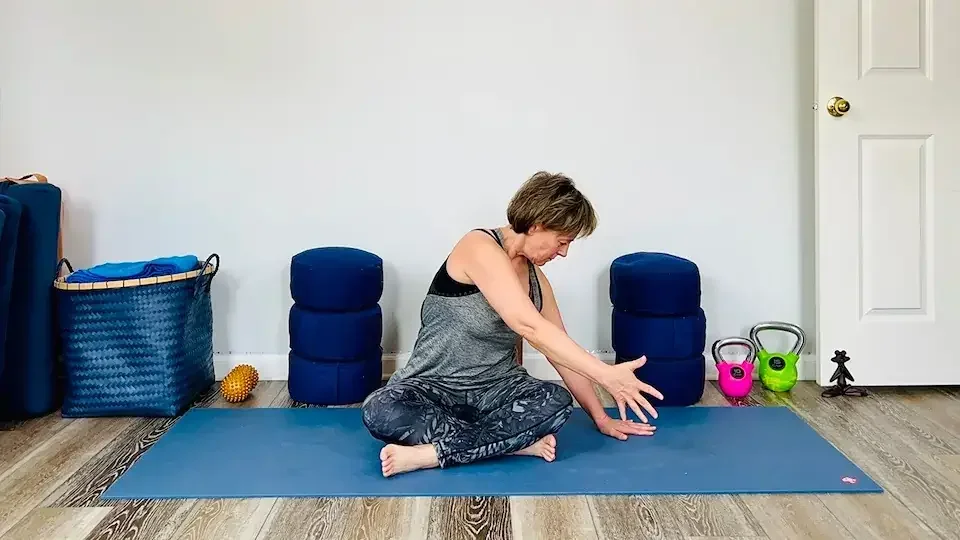 Julie Morrow practicing yoga on a blue mat in a room with white walls, colorful kettlebells and foam rollers.