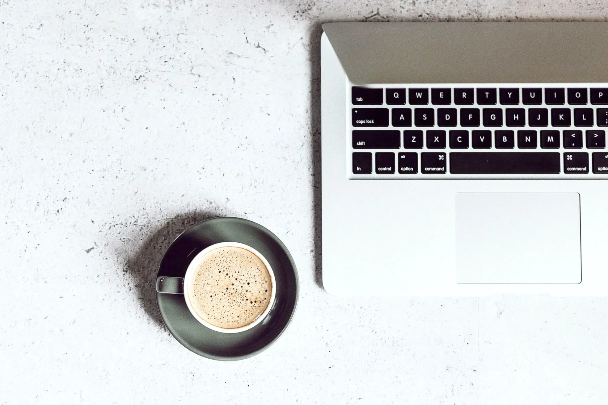 A top-down view of a workspace with a laptop computer and a mug of coffee on a white textured surface.