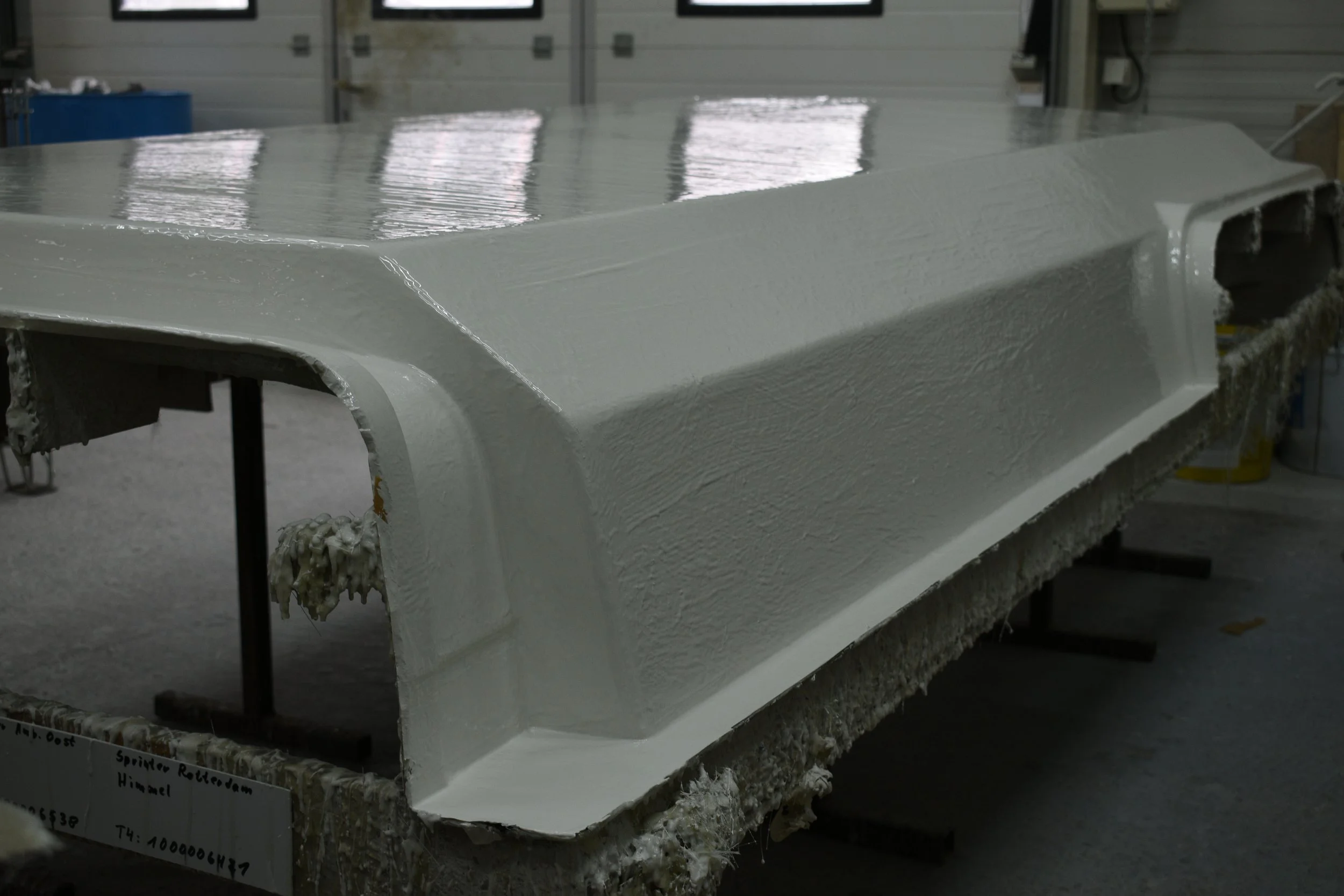 A large white mould for a train component work in progress inside a workshop, with shiny painted gelcoat and visible textures of the material. The mould is on a stand and the background shows a workshop door.