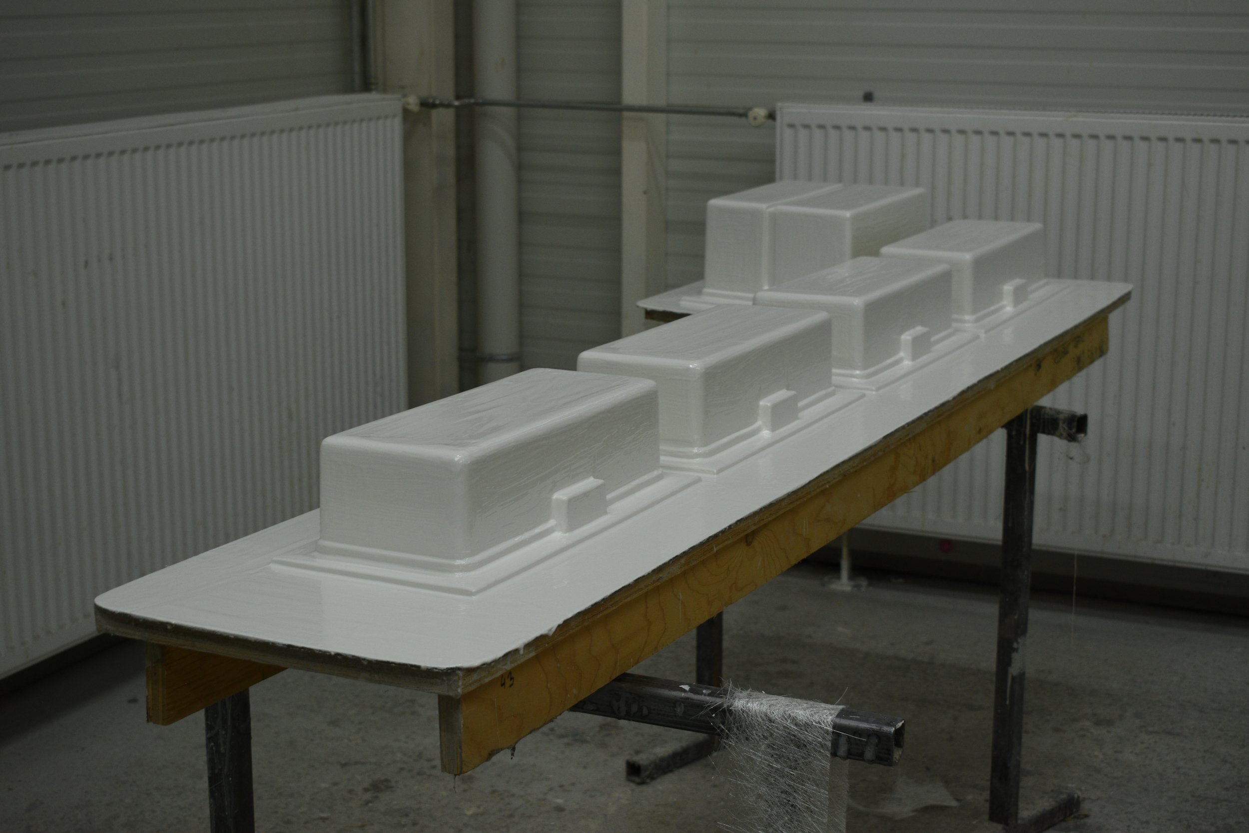 Mould prepared with gelcoat for further laminating composite process on a worktable in a workshop with metal walls and radiators in the background.