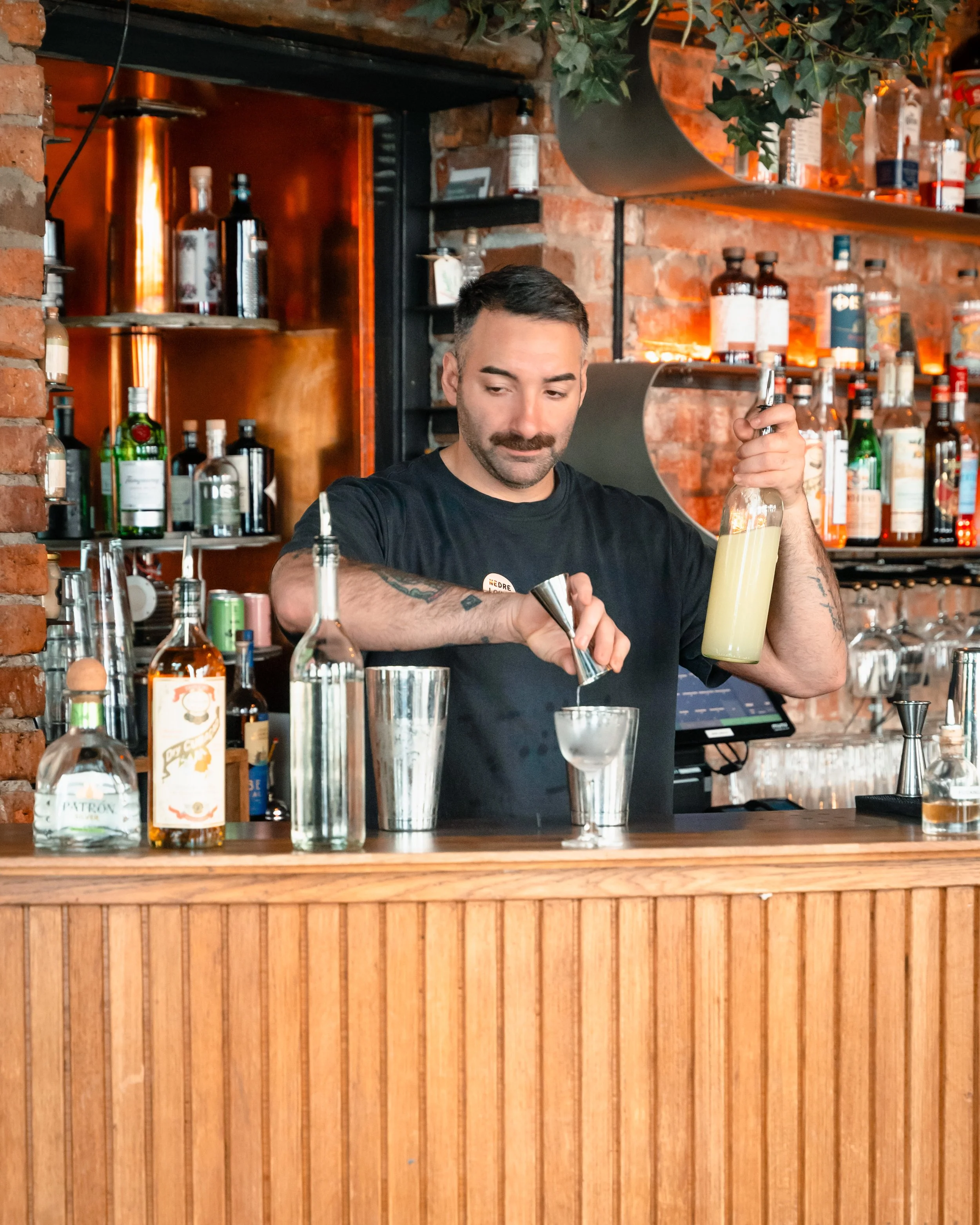 Bartender lager en cocktail på en bar med mange alkoholflasker og glass i bakgrunnen.