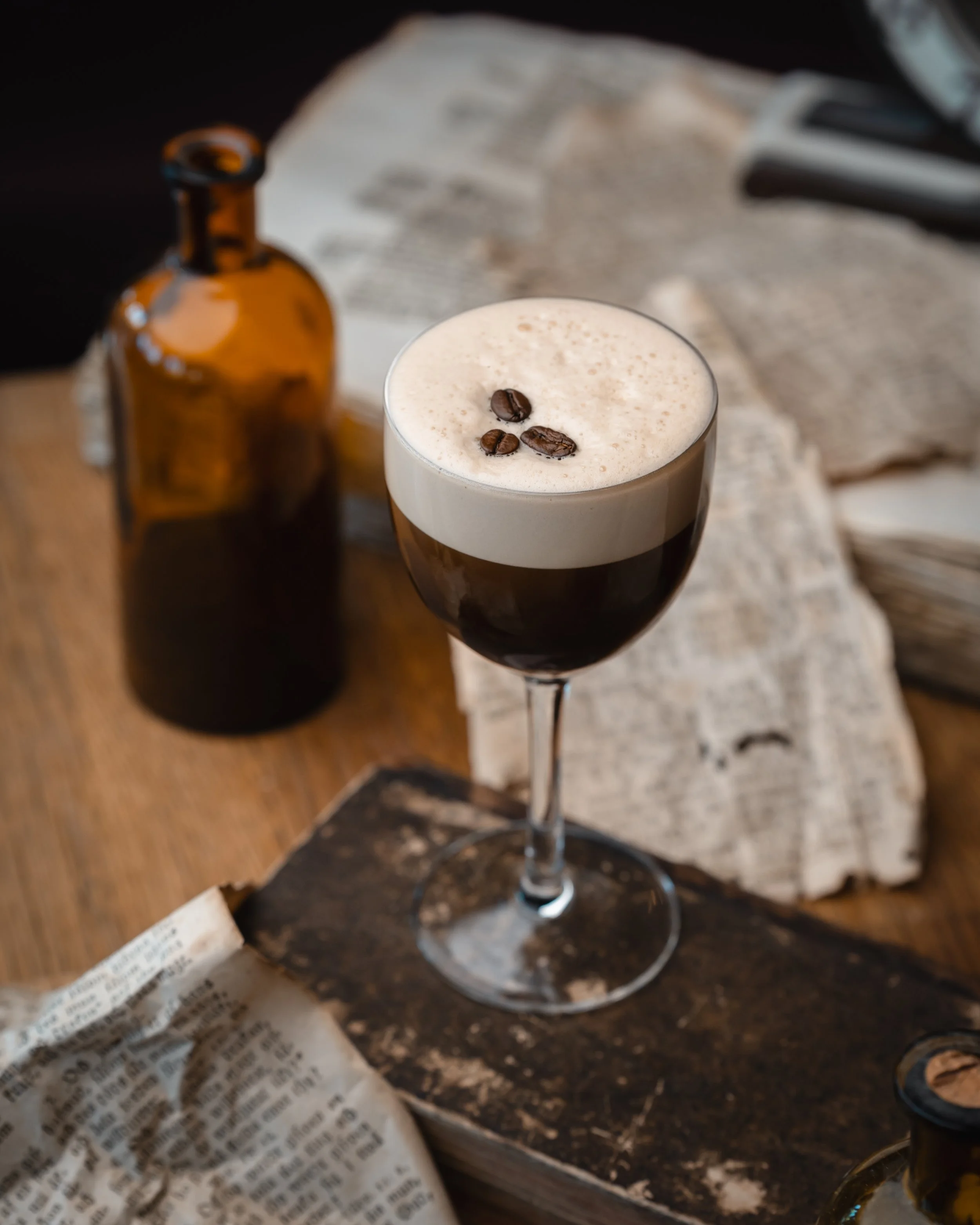 En cocktail med kremaktig topp og tre kaffebønner pyntet på toppen, i et langt glass.