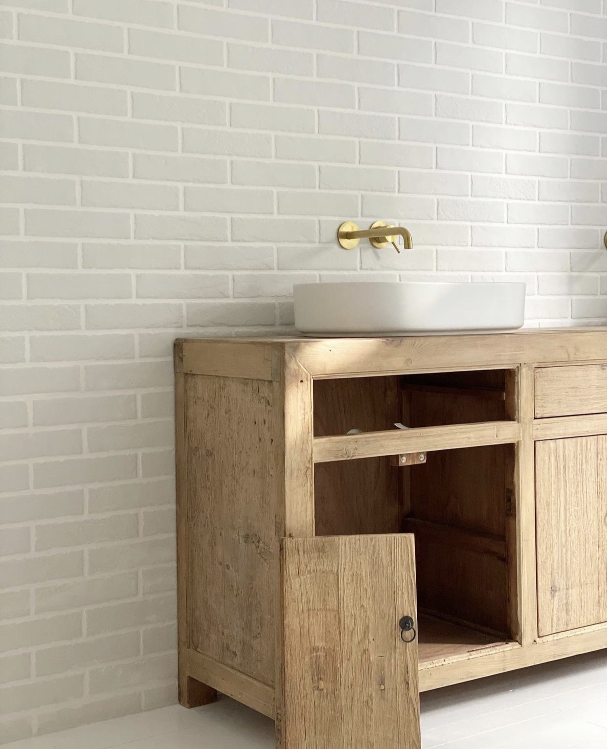 Un meuble en bois avec un évier blanc rond, un robinet mordu en laiton, et un mur en briques blanches.