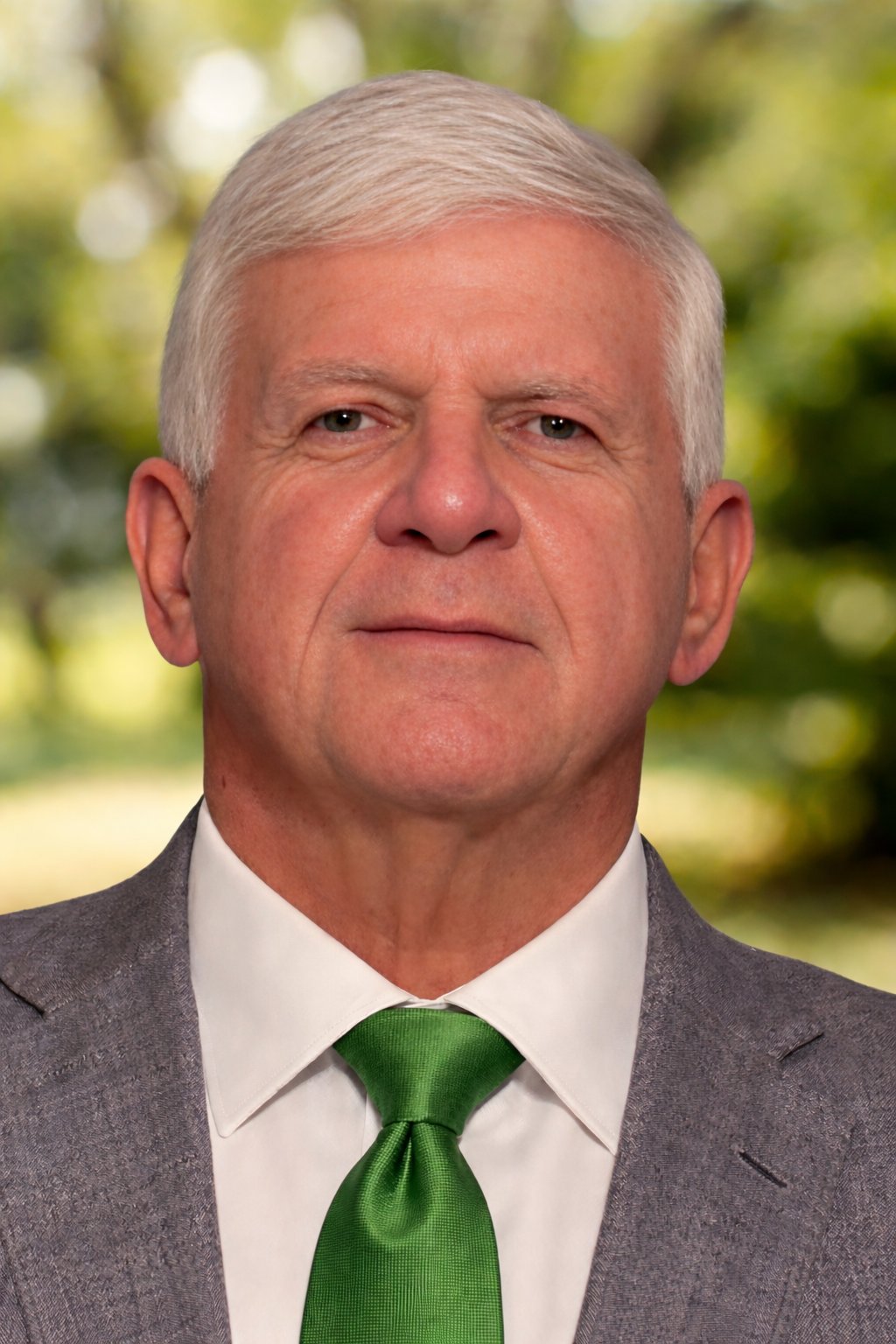 white male in his early 60s in a gray suit with a green tie