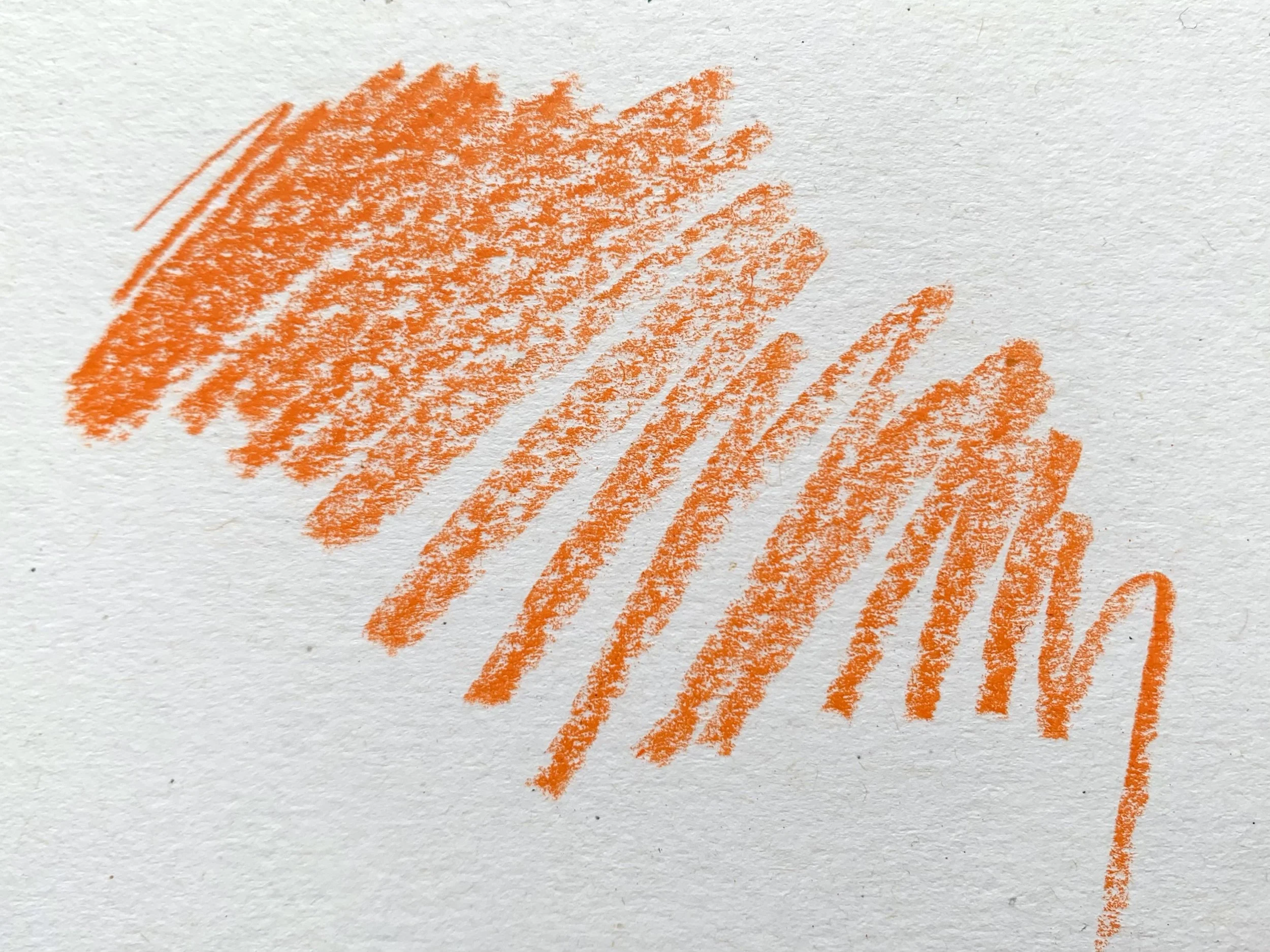 A scribbled test swatch of tangerine orange coloured pencil on textured white paper.