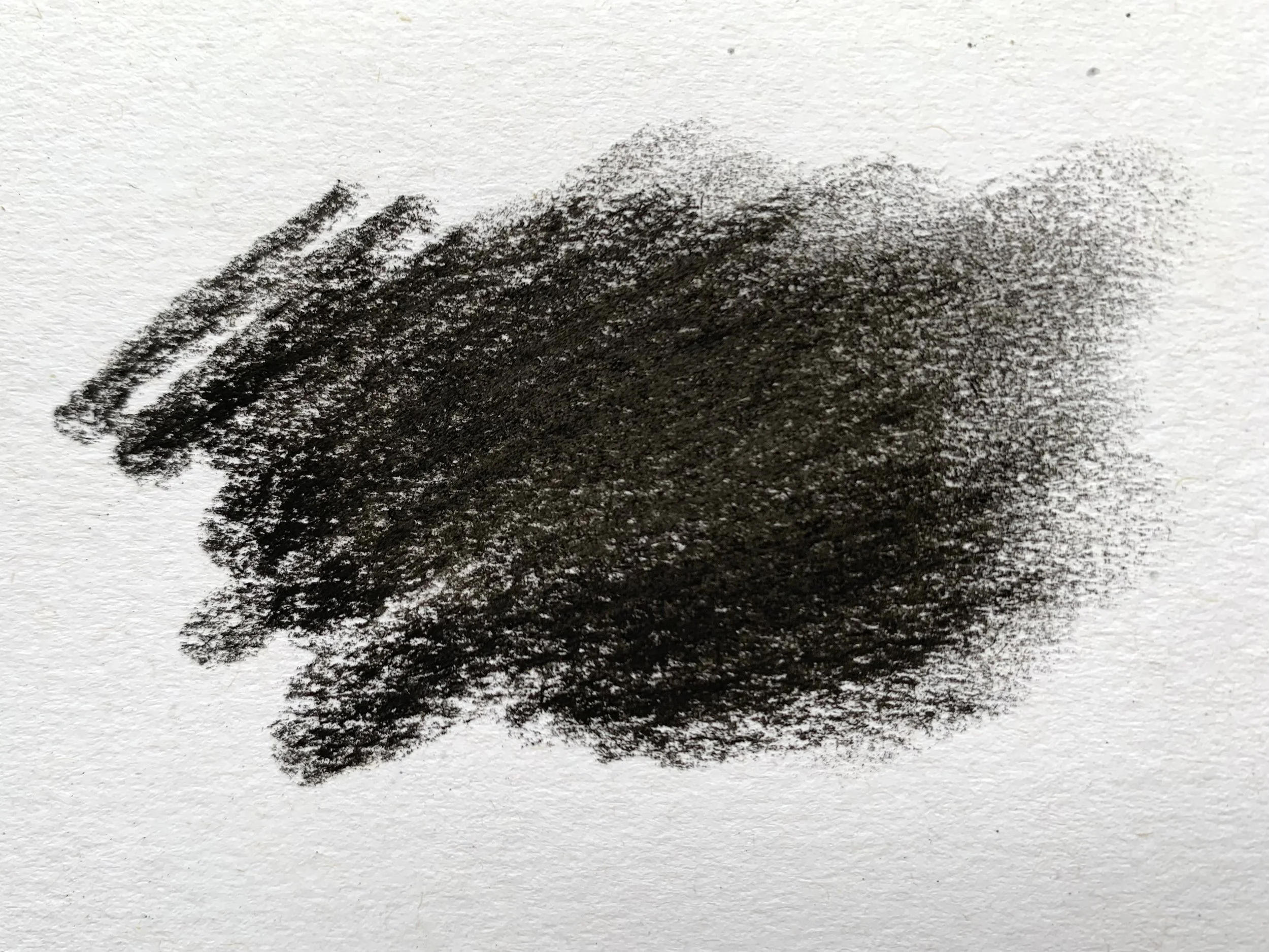 A smudged dark mark made with compressed charcoal on paper with a slight texture.