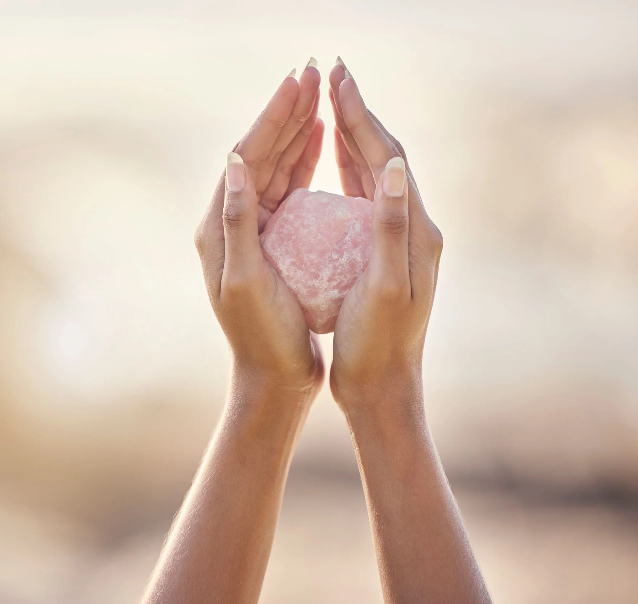 Two hands gently holding a pink salt rock against a bright background, symbolizing balance or healing.