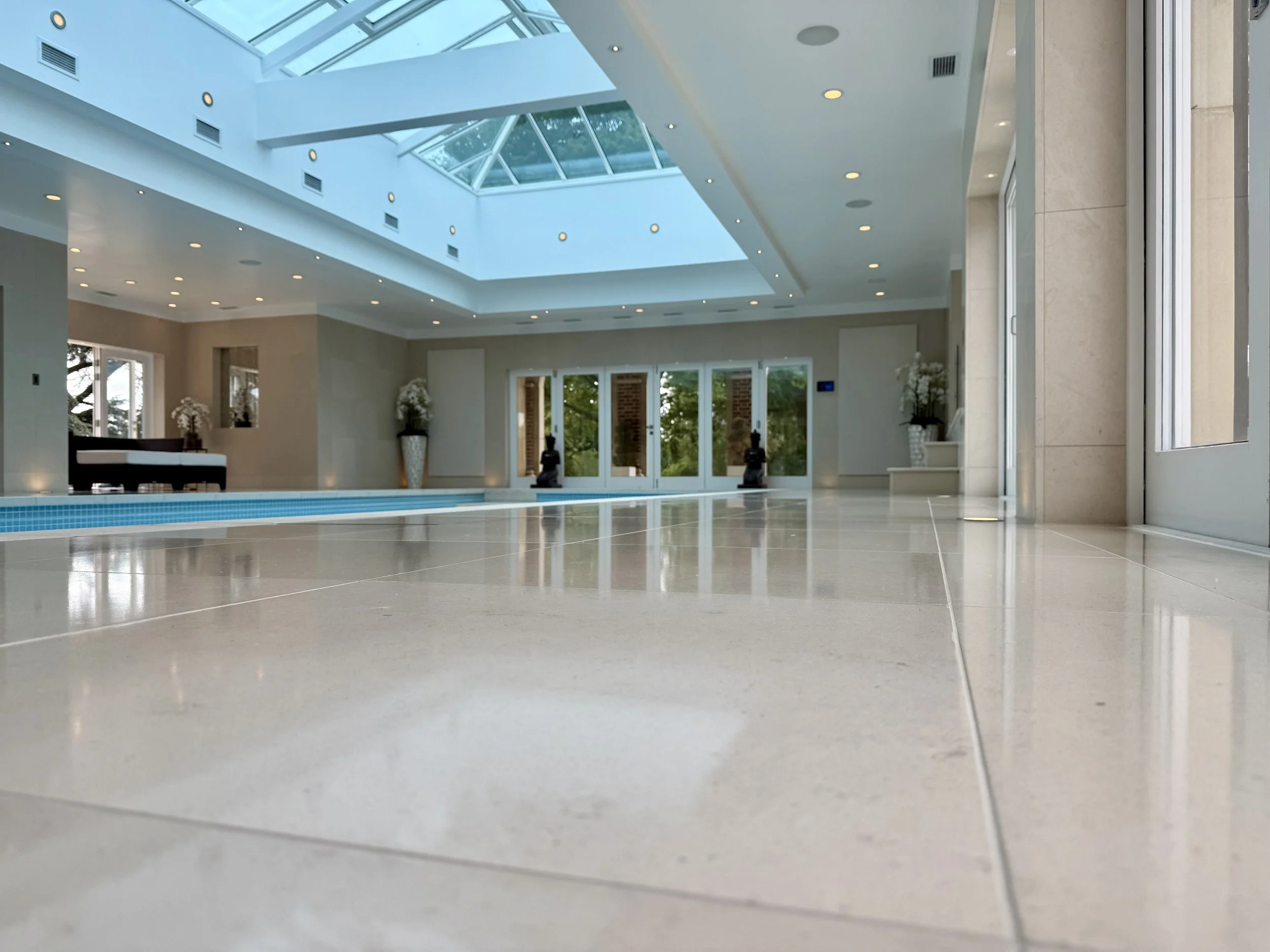 Limestone floor deep-cleaned and polished in a modern indoor pool area with a glass ceiling.