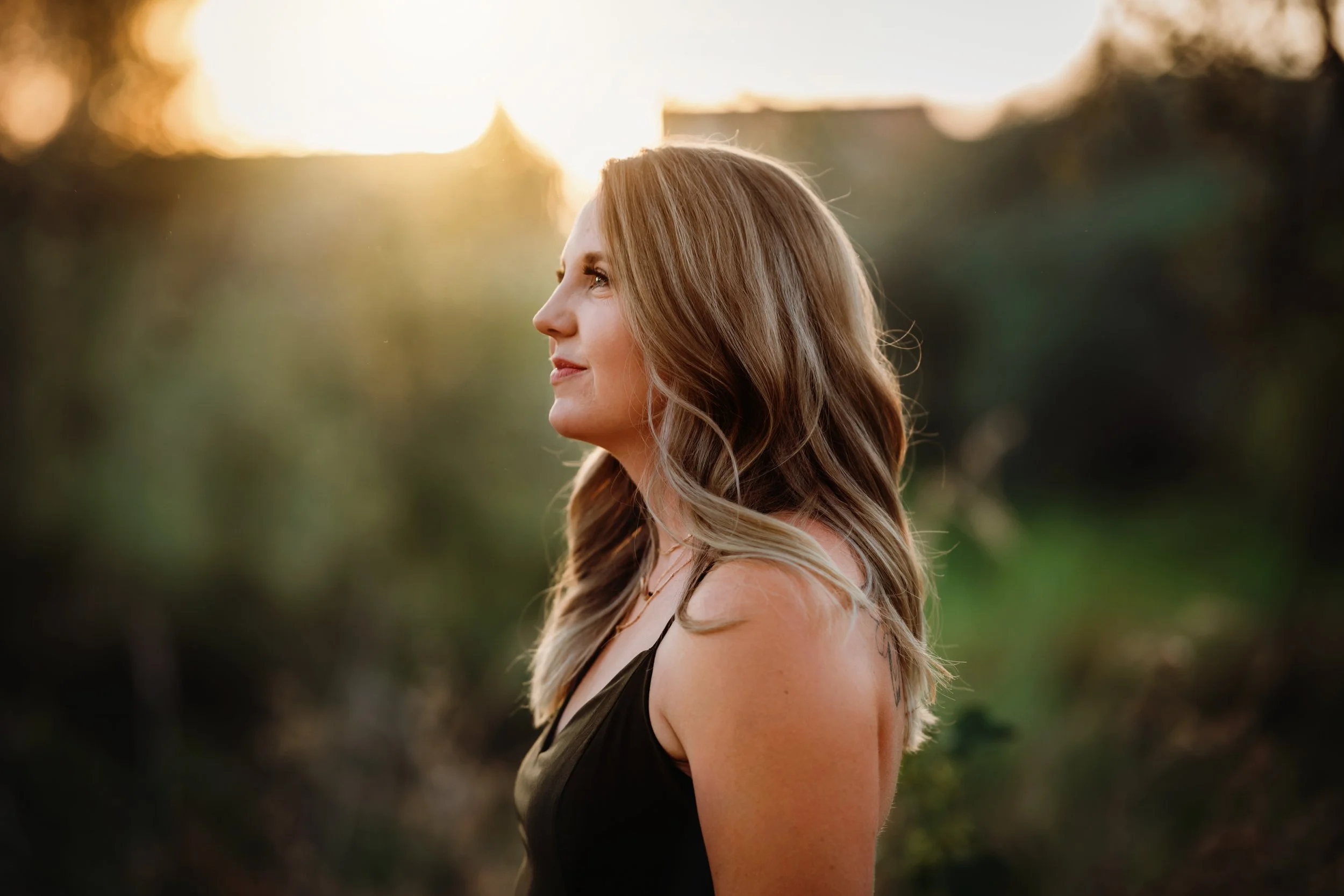 Side profile of a woman with long wavy hair standing outdoors during sunset.