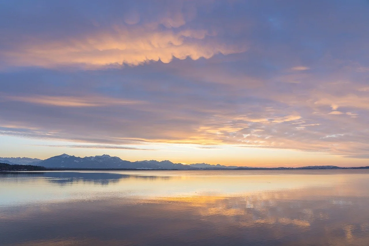 Sunset over mountains and a calm body of water with colorful clouds in the sky