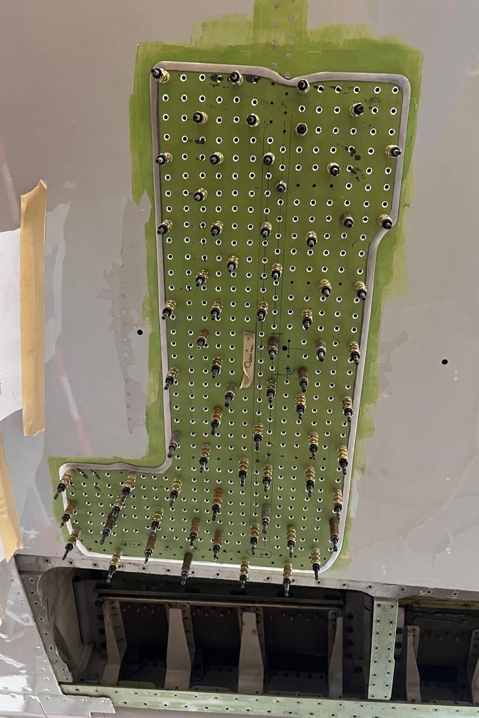 Interior of an aircraft showing a green circuit board with multiple screws and wires installed on the ceiling.