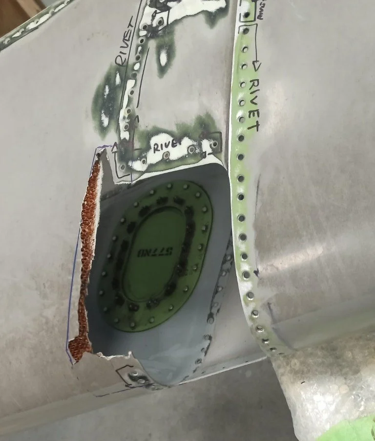Close-up of an aircraft fuselage with a circular inspection panel and handwritten notes indicating 'RIVER' and labeled rivets along seams.