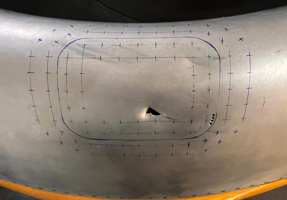 A metallic surface with a rectangular outline and various measurement markings in purple and green, along with a small black triangular object near the center.