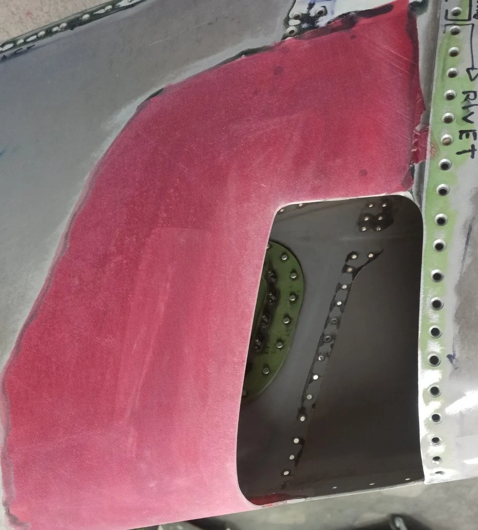 Close-up of an aircraft fuselage with a red covering on part of the metal body and visible rivets.