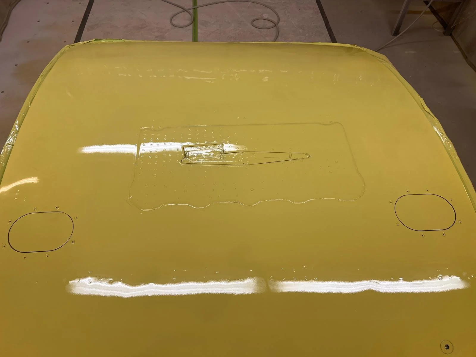 Yellow aircraft panel with access panels and a thin metallic rod on the surface.