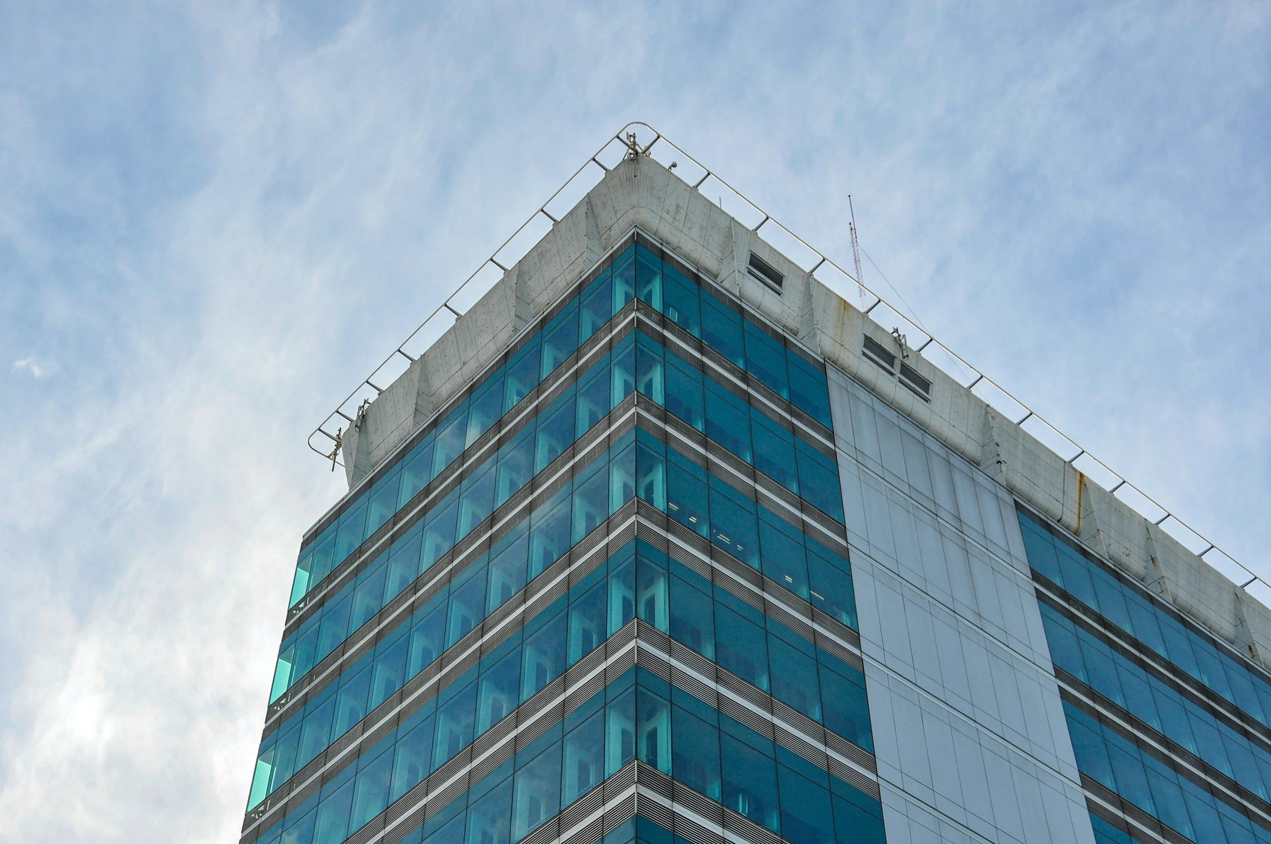 A tall modern office building with a glass facade under a cloudy sky.