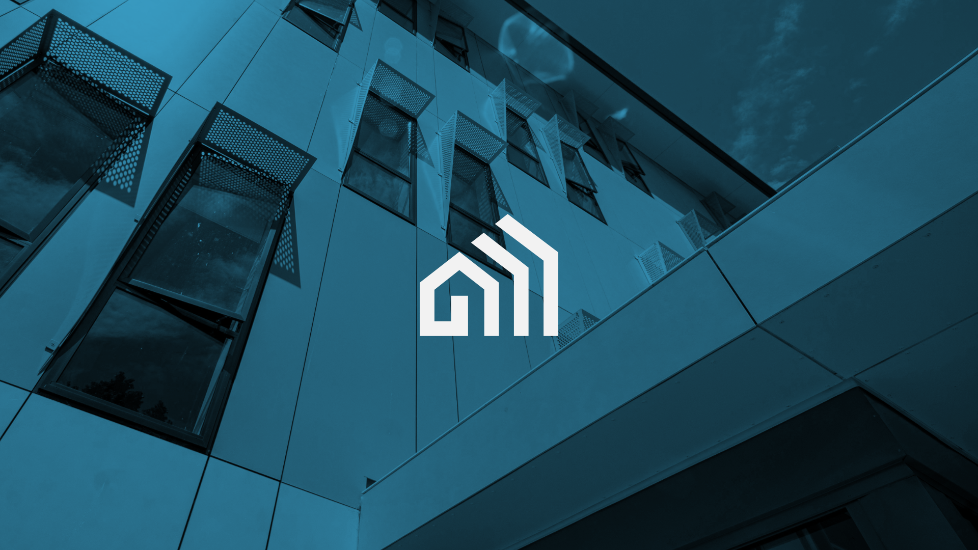 Modern building with reflective glass windows and metal exterior panels, with a logo featuring a stylized house and bars in the foreground.