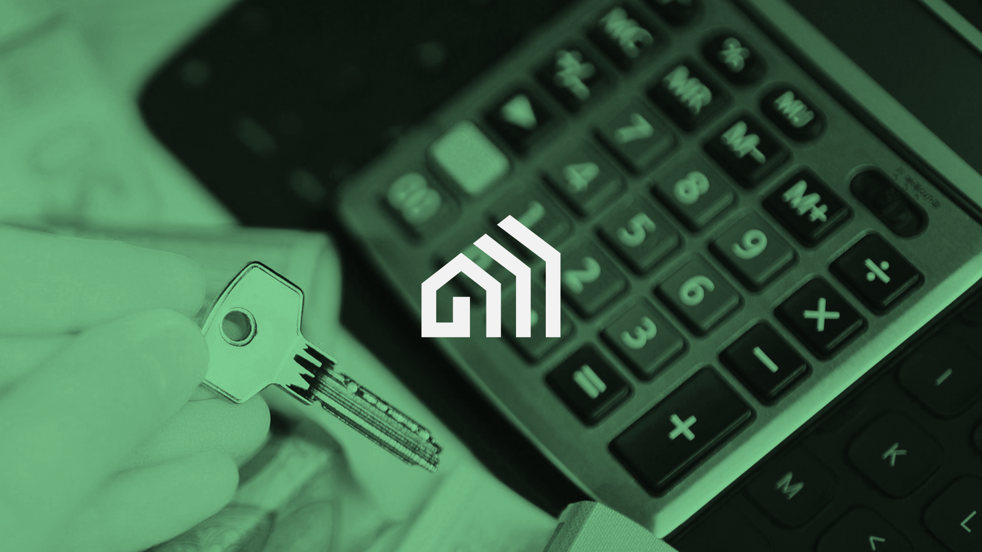 A hand holding a key near a calculator on a desk.
