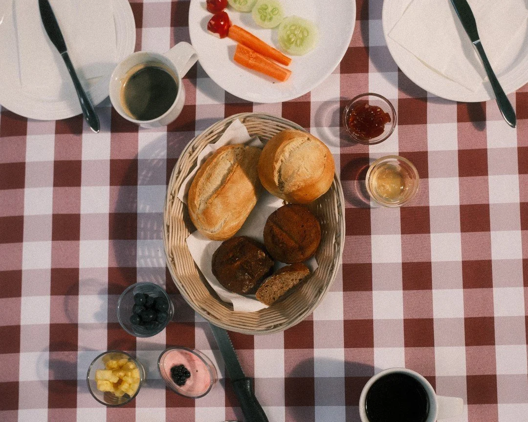 Frühstückstisch mit Brötchen, Butter, Marmelade, verschiedenen Aufschnitt, Kaffee, Joghurt mit Beeren, Obst und Gemüse
