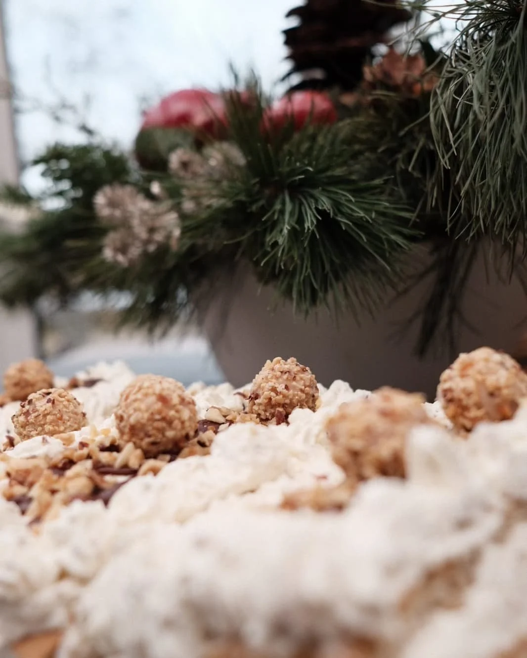 Nahaufnahme von weißen Weihnachtskeksen mit Nüssen und Schokoladenstückchen. Im Hintergrund eine Tafel mit Tannenzweigen, roten und weißen Dekorationen.